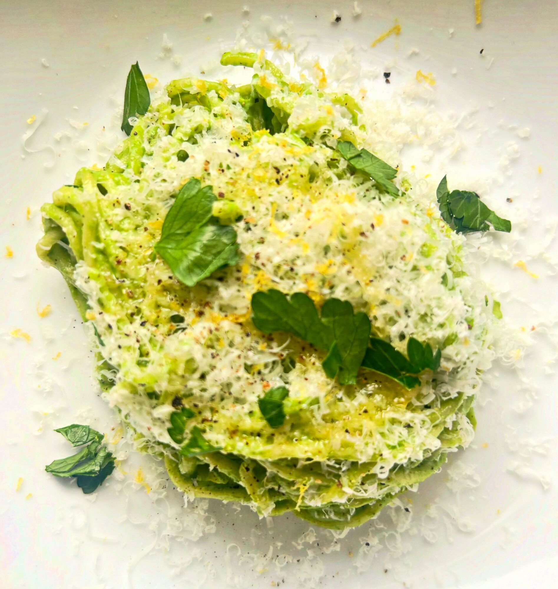 A plate of pasta with green sauce, topped with grated cheese and fresh basil leaves.