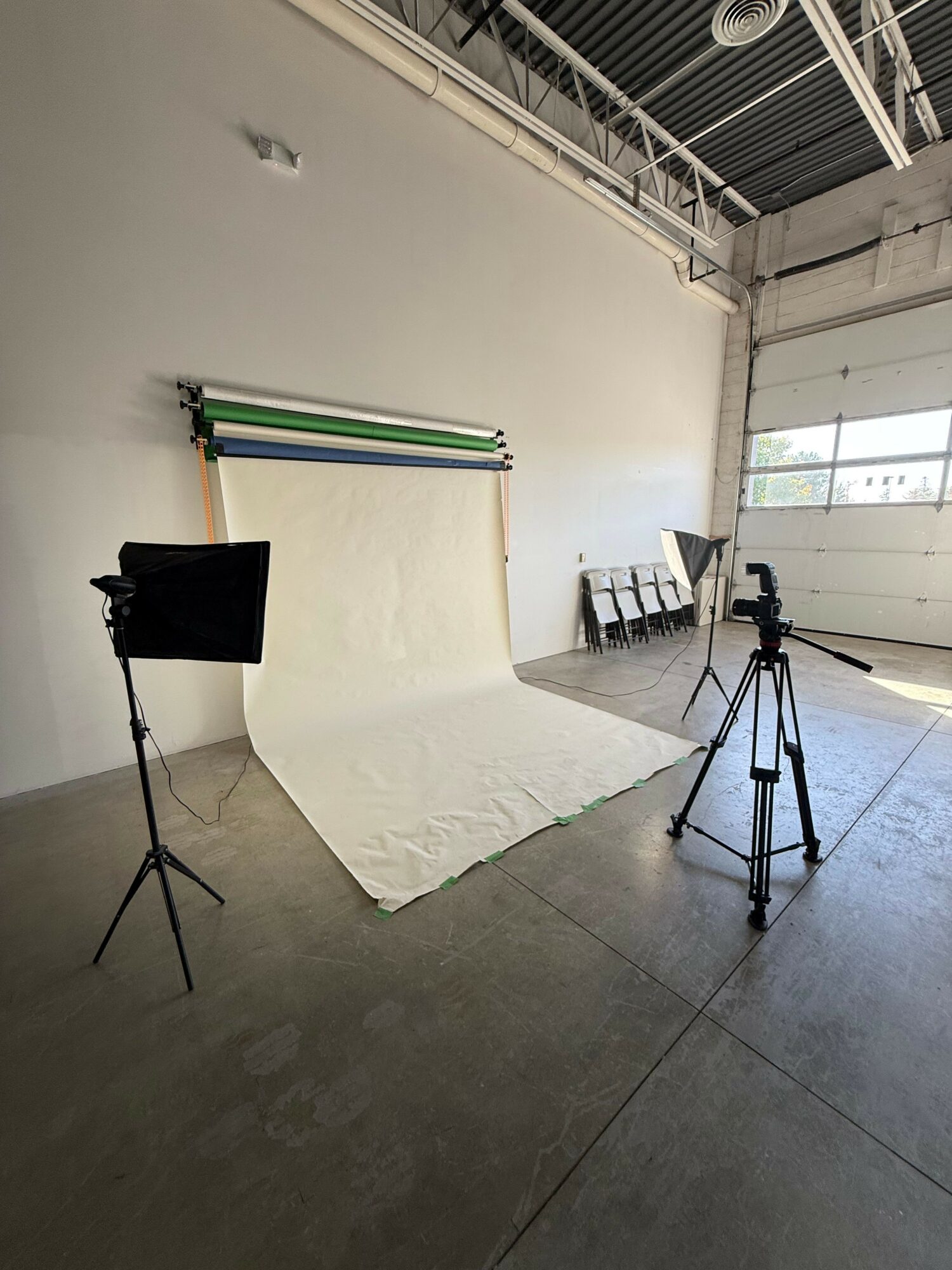 Photography setup with a backdrop, tripod, and lighting equipment in a room with concrete floor and white walls.