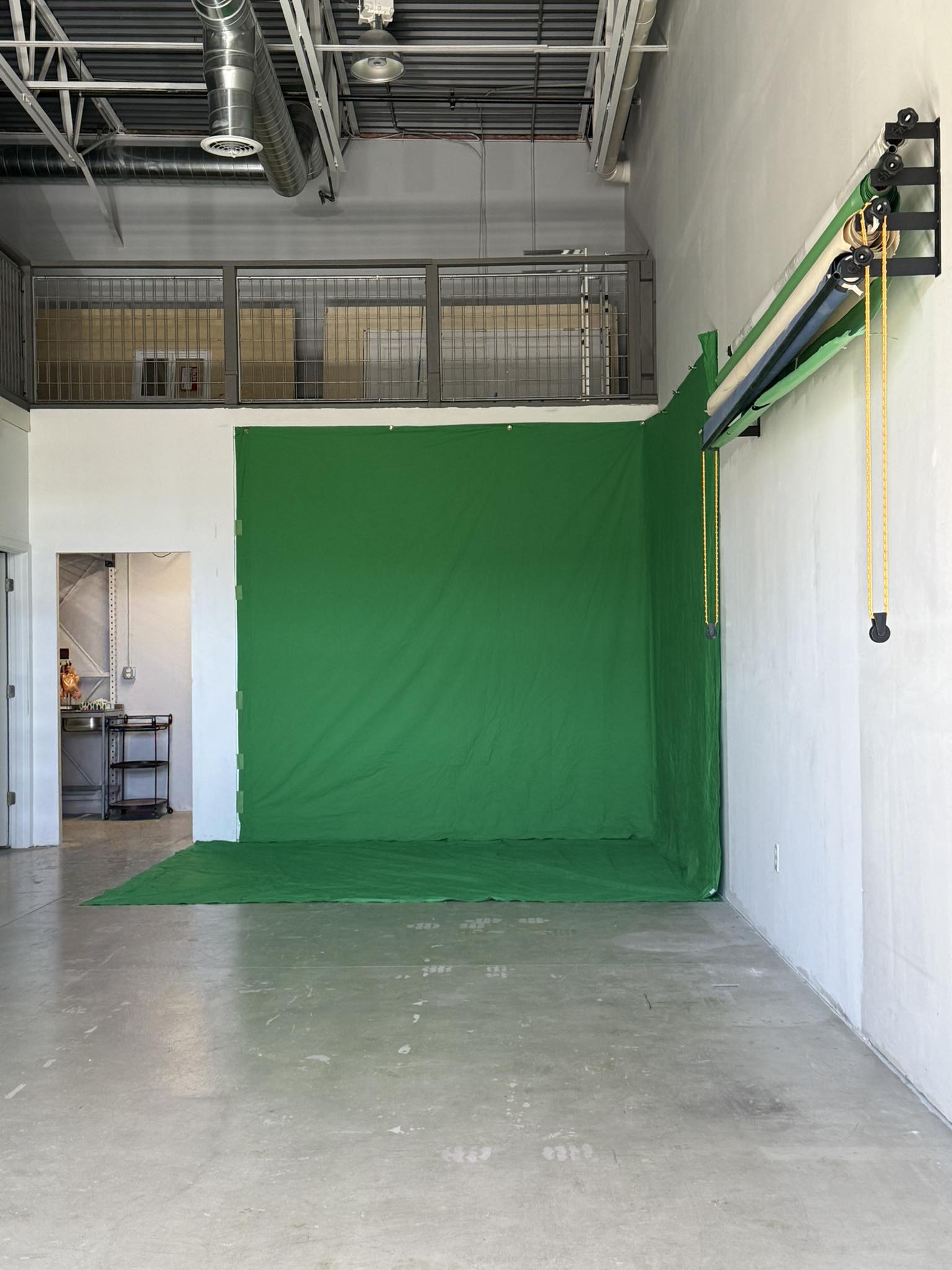 Green screen backdrop in an industrial space with pipes and a small doorway, floor and wall visible.