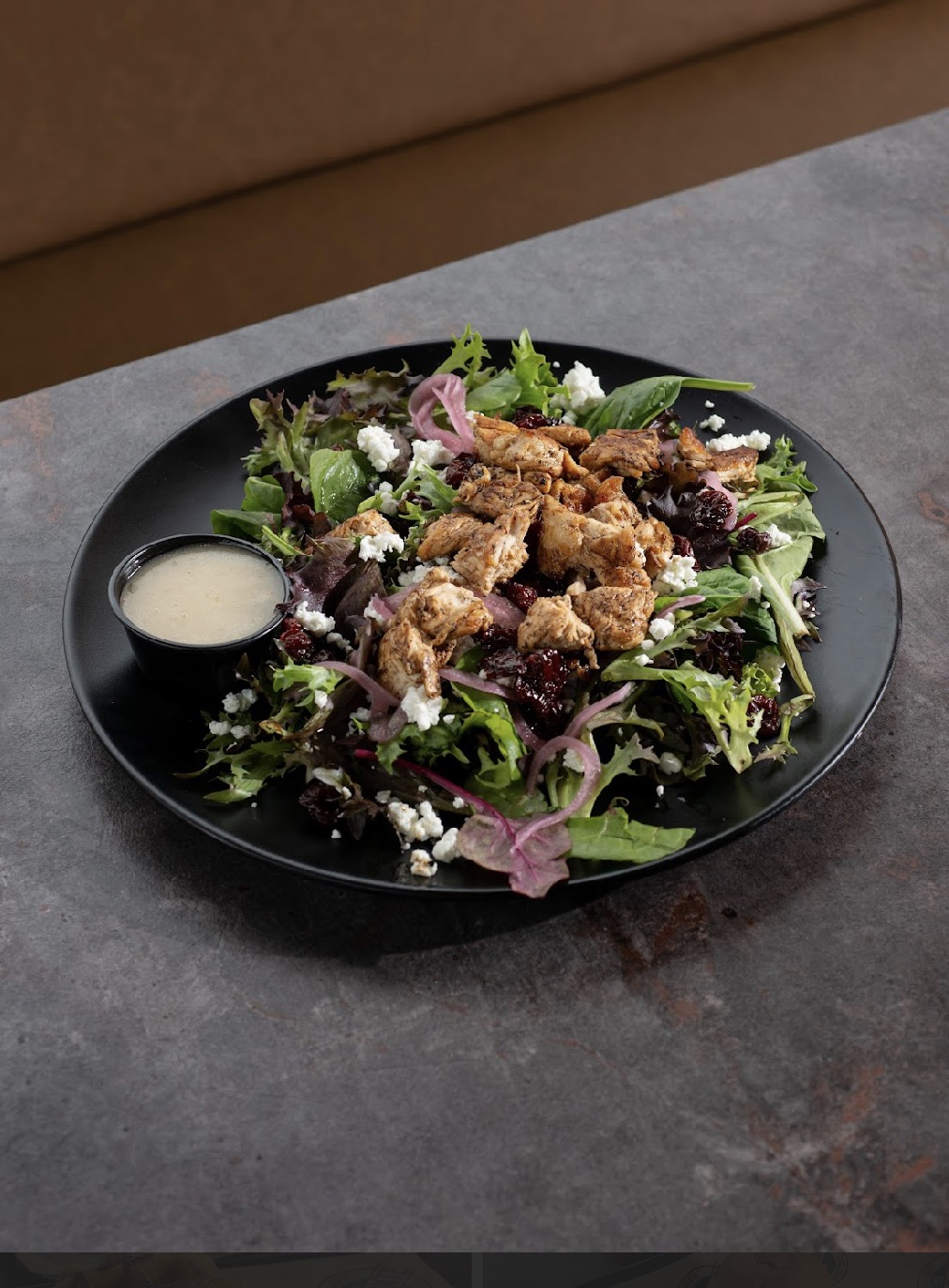 Salad with fried chicken pieces, purple onions, greens, and a small cup of dressing on a black plate.