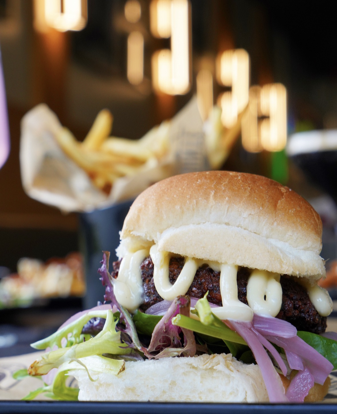 Hamburger with lettuce, onions, and sauce on a bun, served with a side of fries in the background.