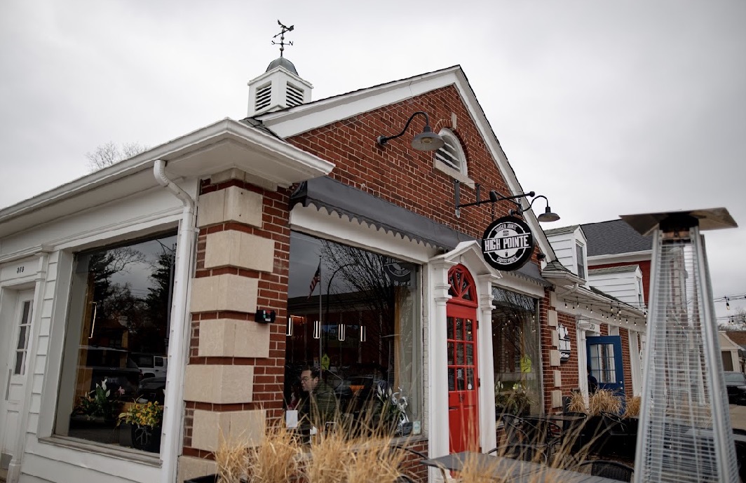 Brick building with a red door, large window, and a sign hanging outside, under a cloudy sky.