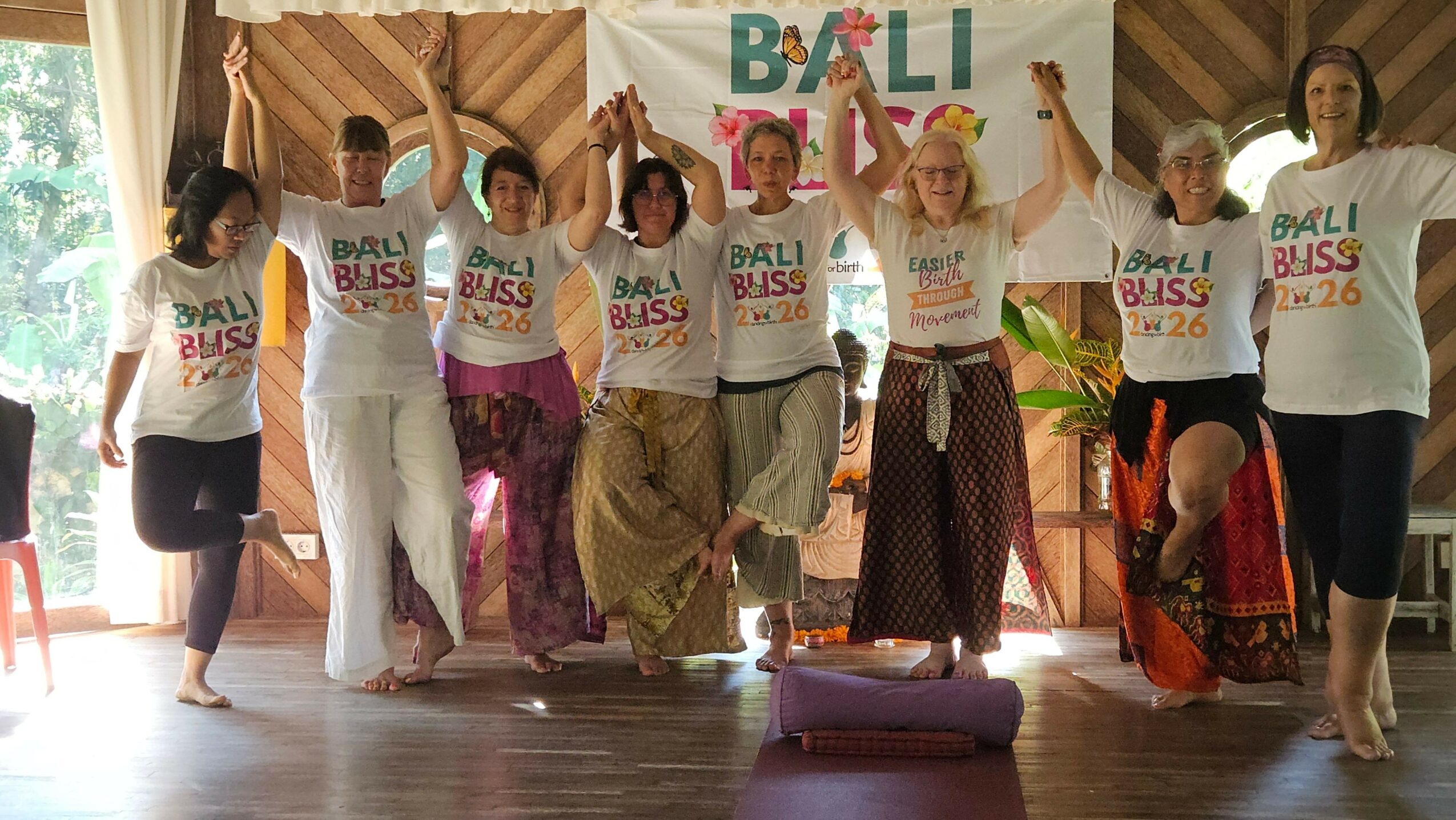 Group of people holding banners and signs, standing indoors with wooden walls and windows, some waving and smiling.