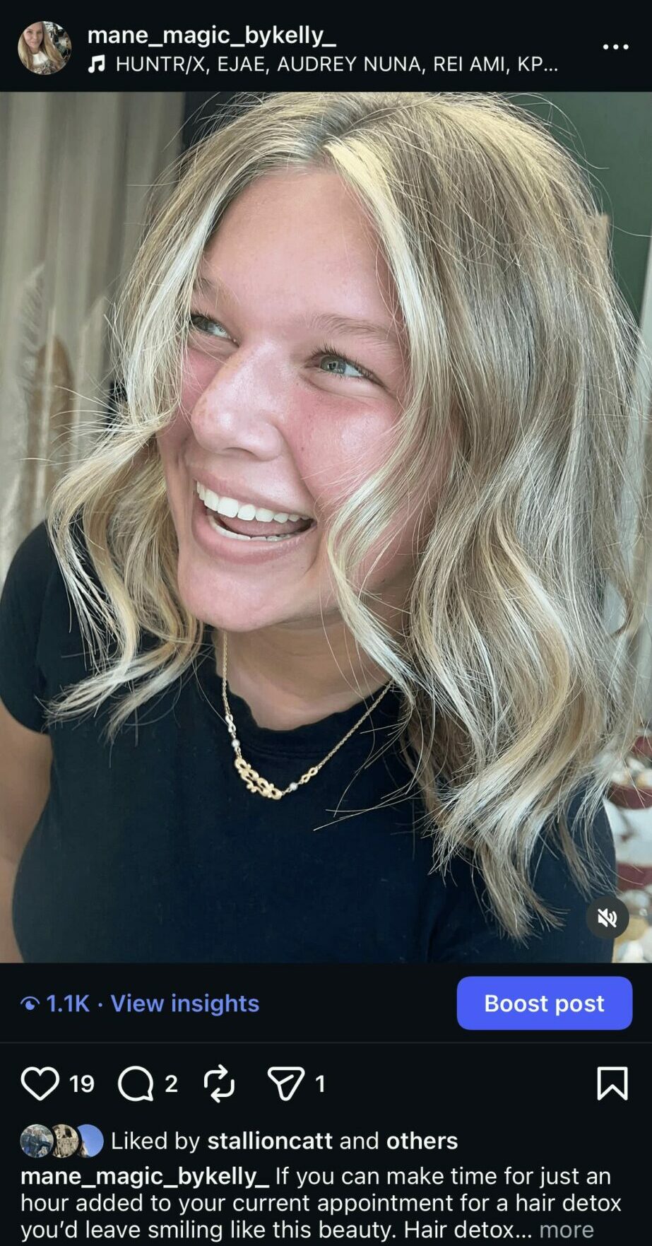 Young woman with blonde wavy hair smiling, wearing a black top and layered necklaces.