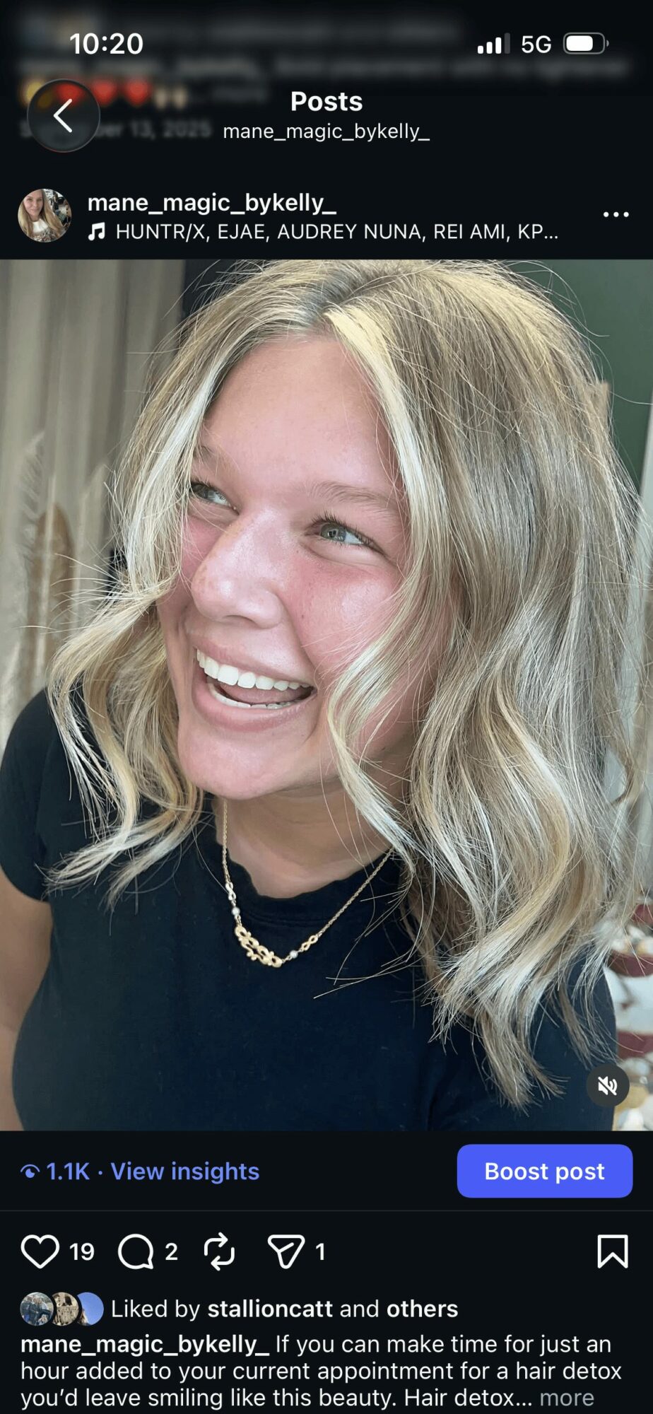 Young woman with blonde wavy hair smiling, wearing a black top and layered necklaces.
