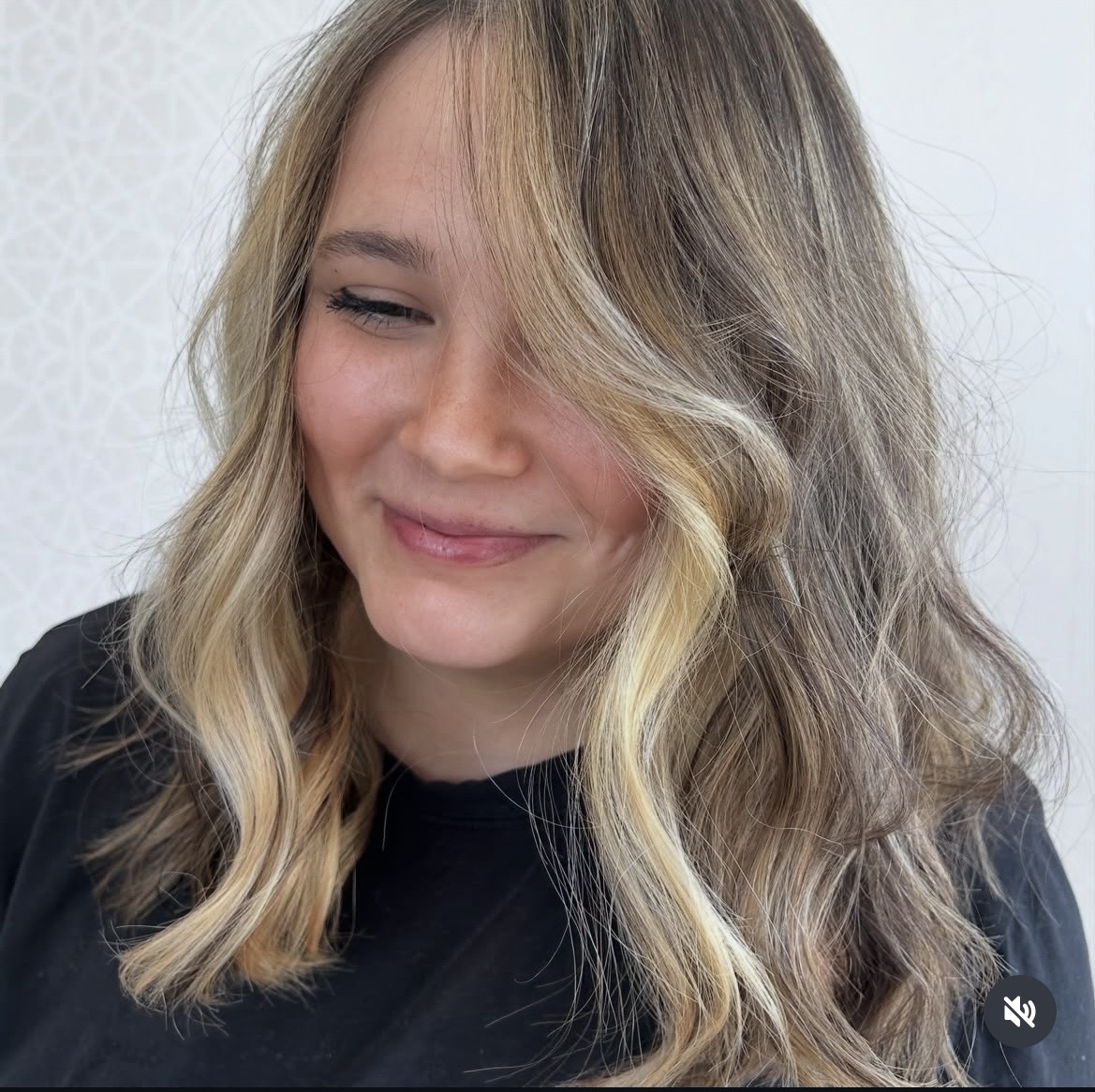 Woman with wavy blonde hair smiling, wearing a black top, against a light background.
