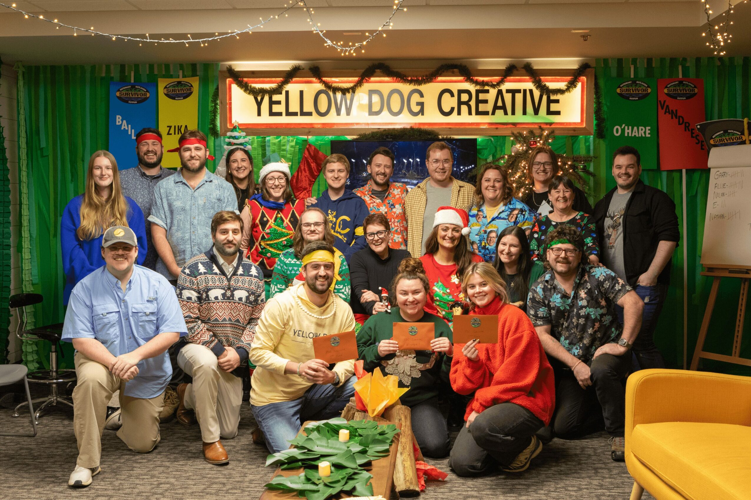 Group of people on stage with a sign reading 'YELLOW DOG CREATIVE', colorful curtains, and festive decorations, smiling and posing.
