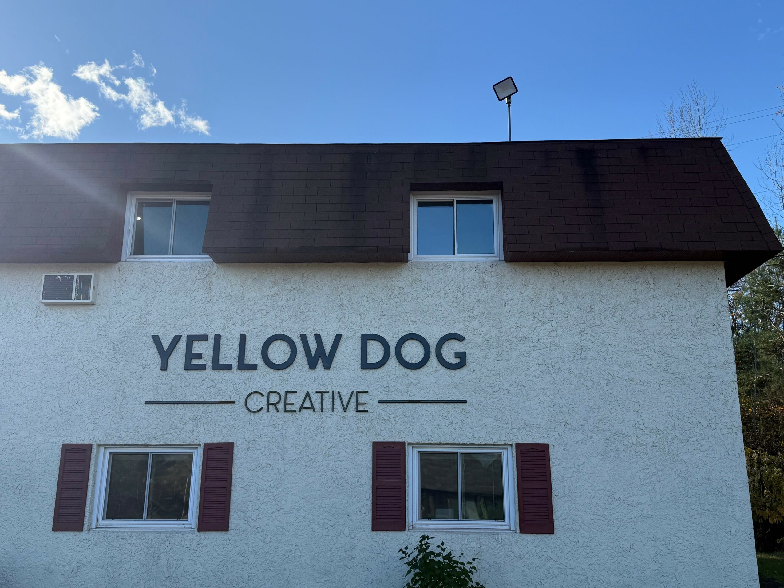 Building with a sign reading 'YELLOW DOG CREATIVE' and two windows with shutters, under a blue sky.