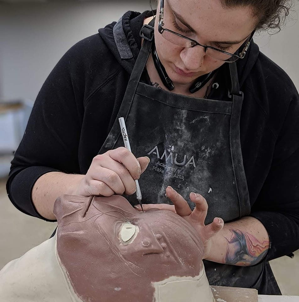 Person wearing glasses and apron drawing on a large animal sculpture with a marker, focusing on the work.