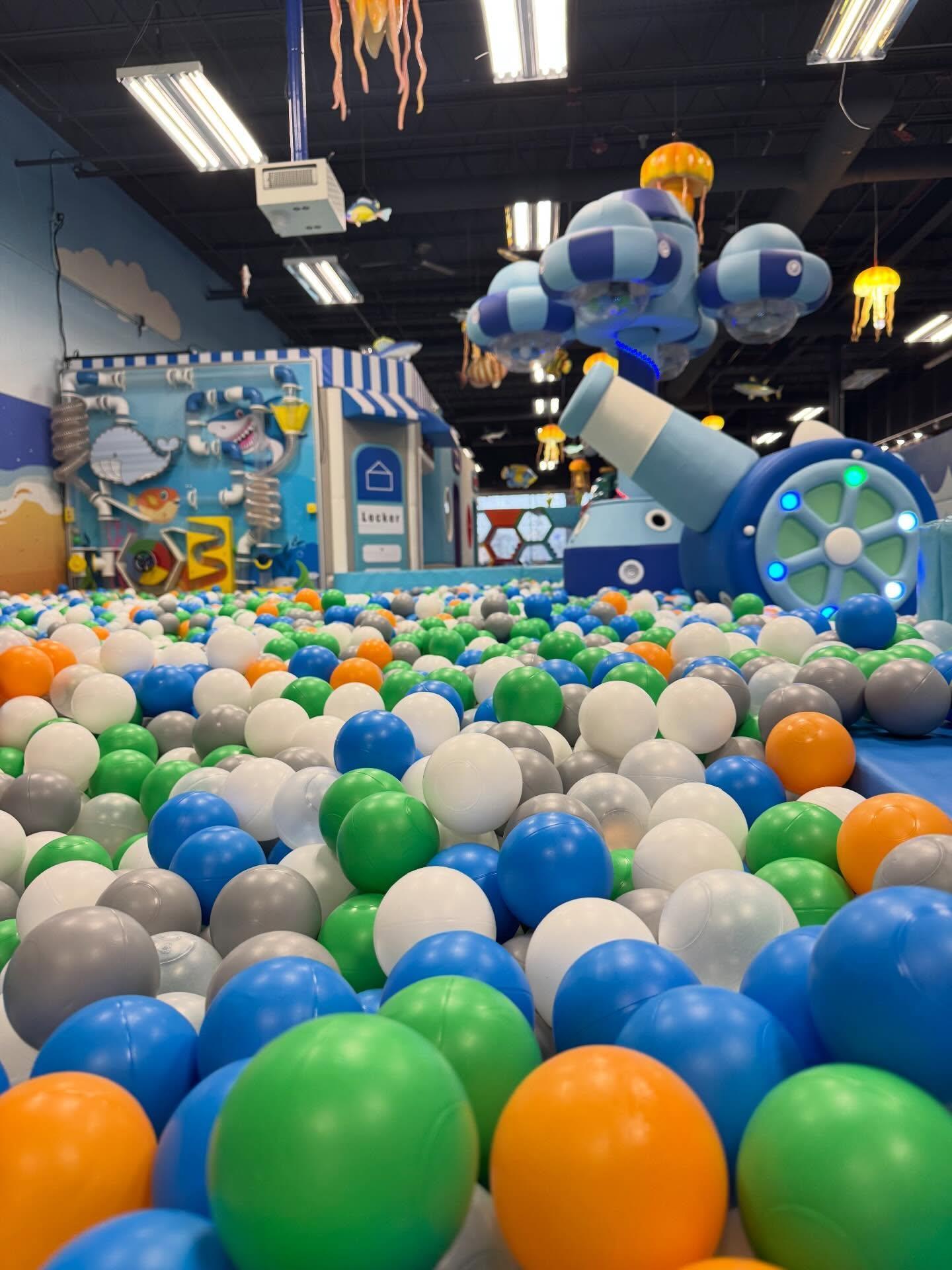 Indoor play area with colorful plastic balls, a large blue and white robot, and playful decorations.