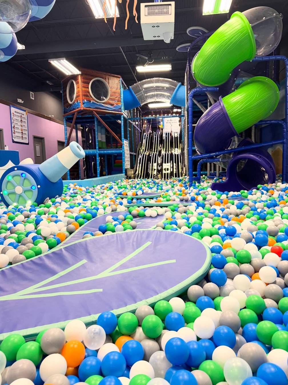 Indoor playground with ball pit, slides, and play structures, filled with colorful balls and play equipment.