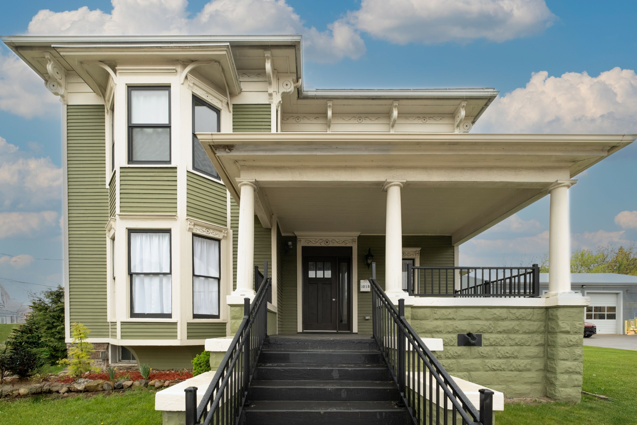 Front view of a house with a porch, stairs, and a bay window, under a partly cloudy sky.