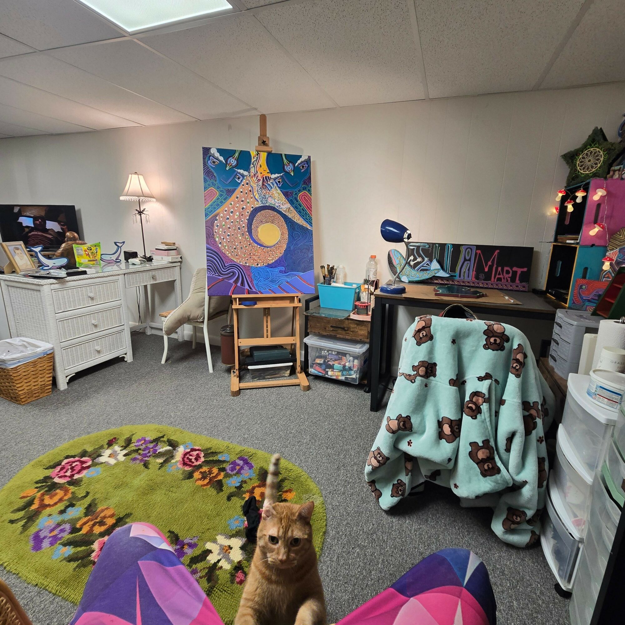 Room with a colorful painting, a small wooden stool, a white cabinet, and a dog on a floral rug.