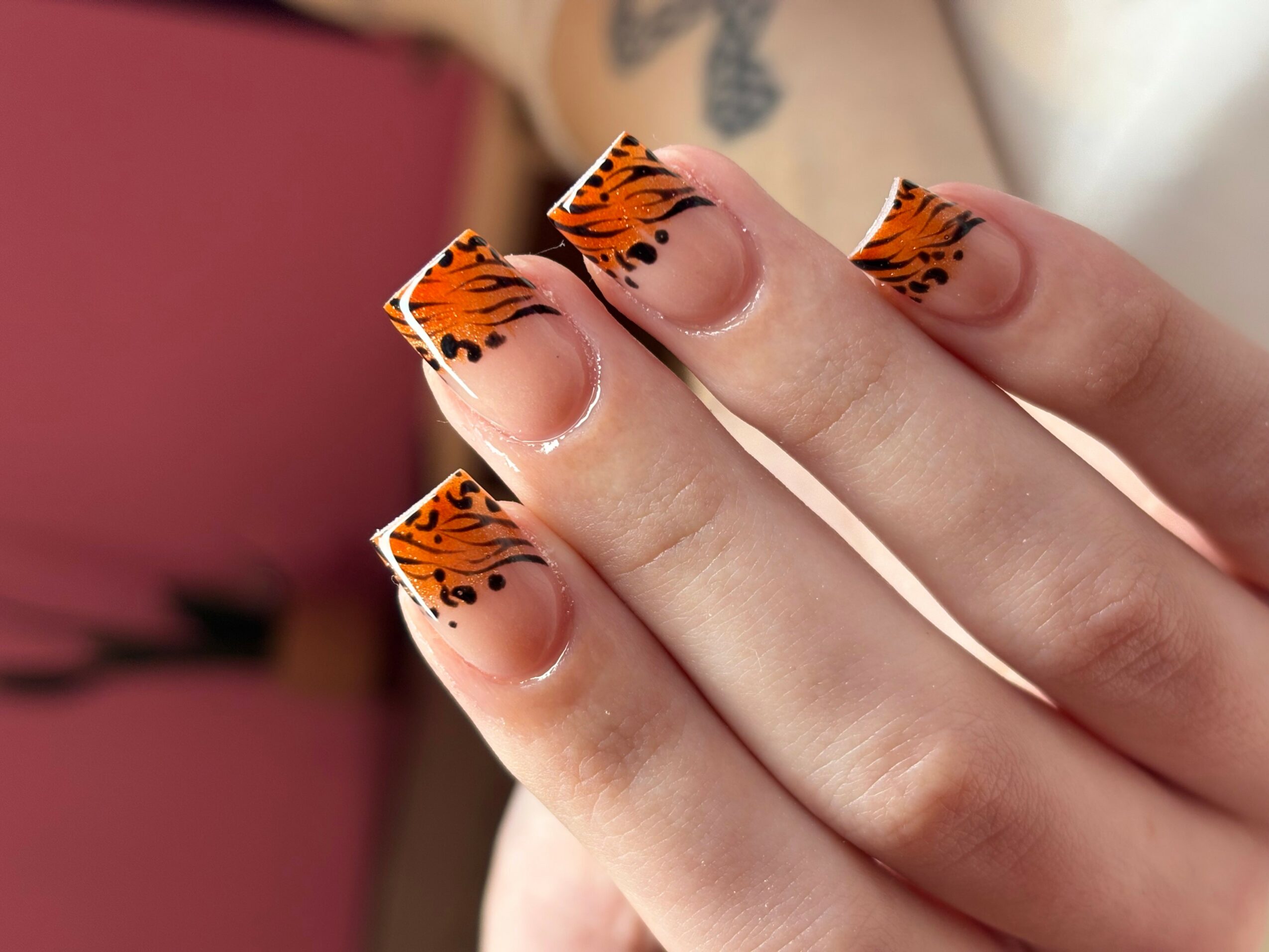 Close-up of fingers with tiger-striped nail art on nails, with a blurred background.