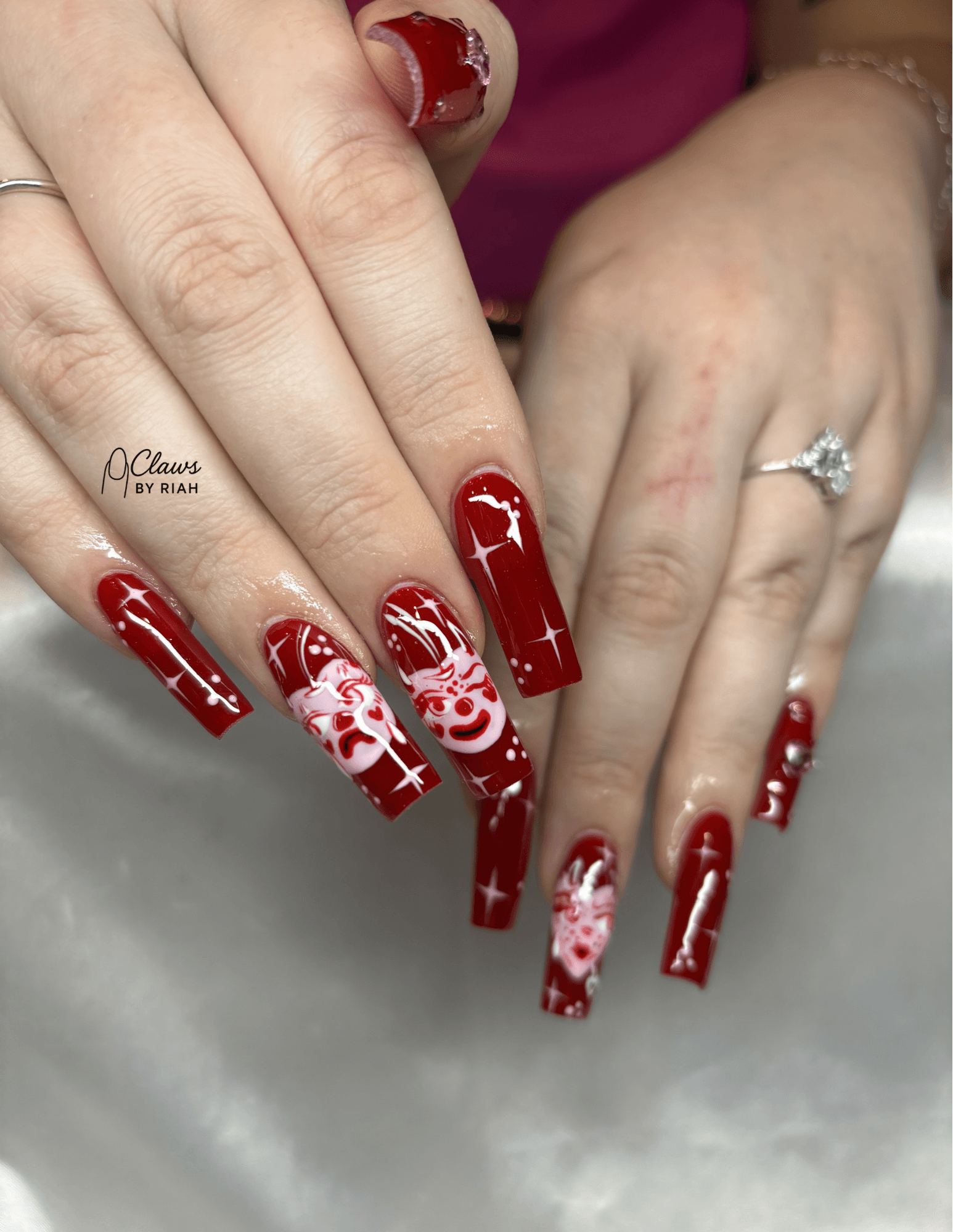Hands with red and white Christmas-themed nail art, including reindeer and snowflakes, one hand with a ring, nails long and decorated.