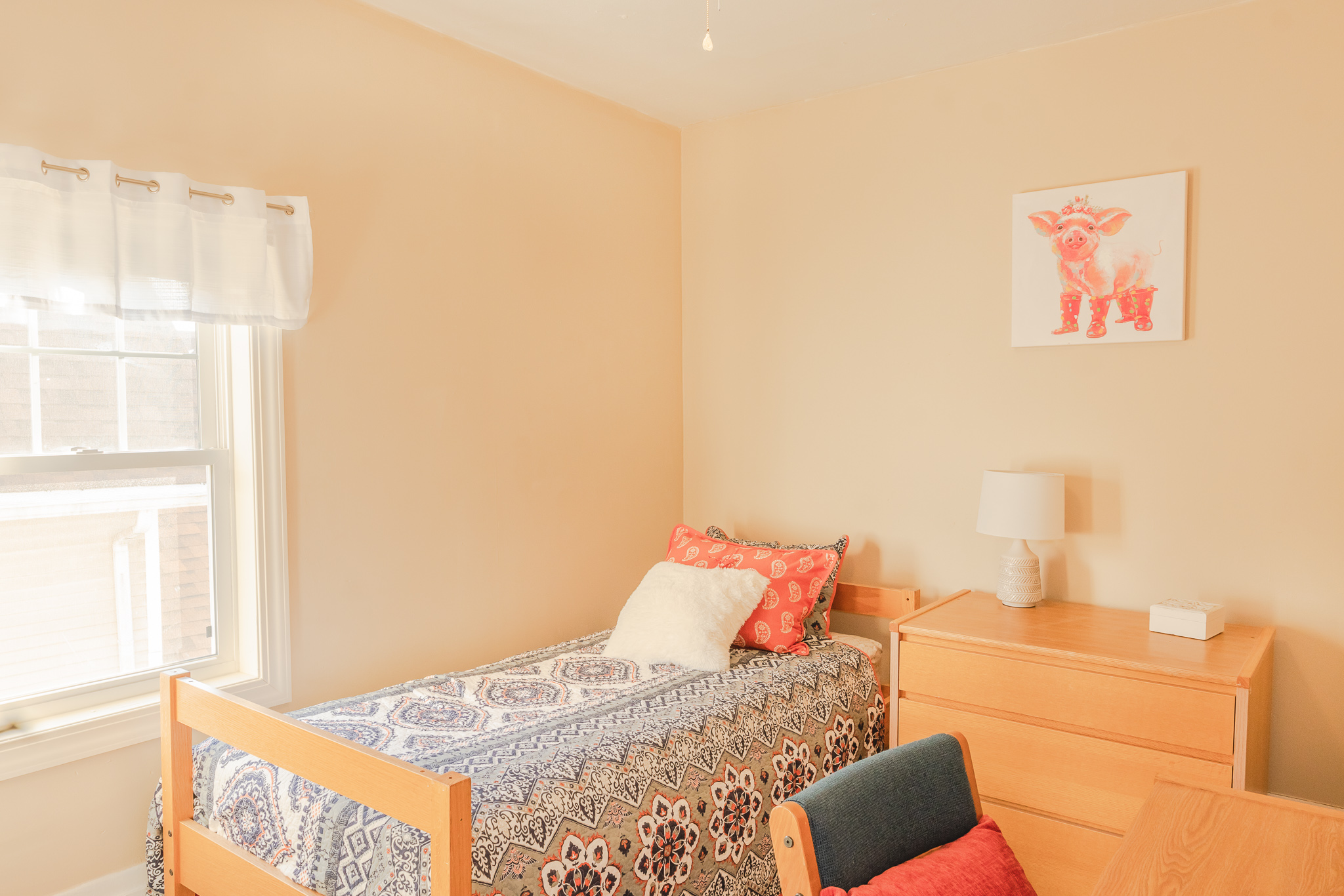 Bedroom with a bed, dresser, window, and wall art, featuring neutral and pastel colors.
