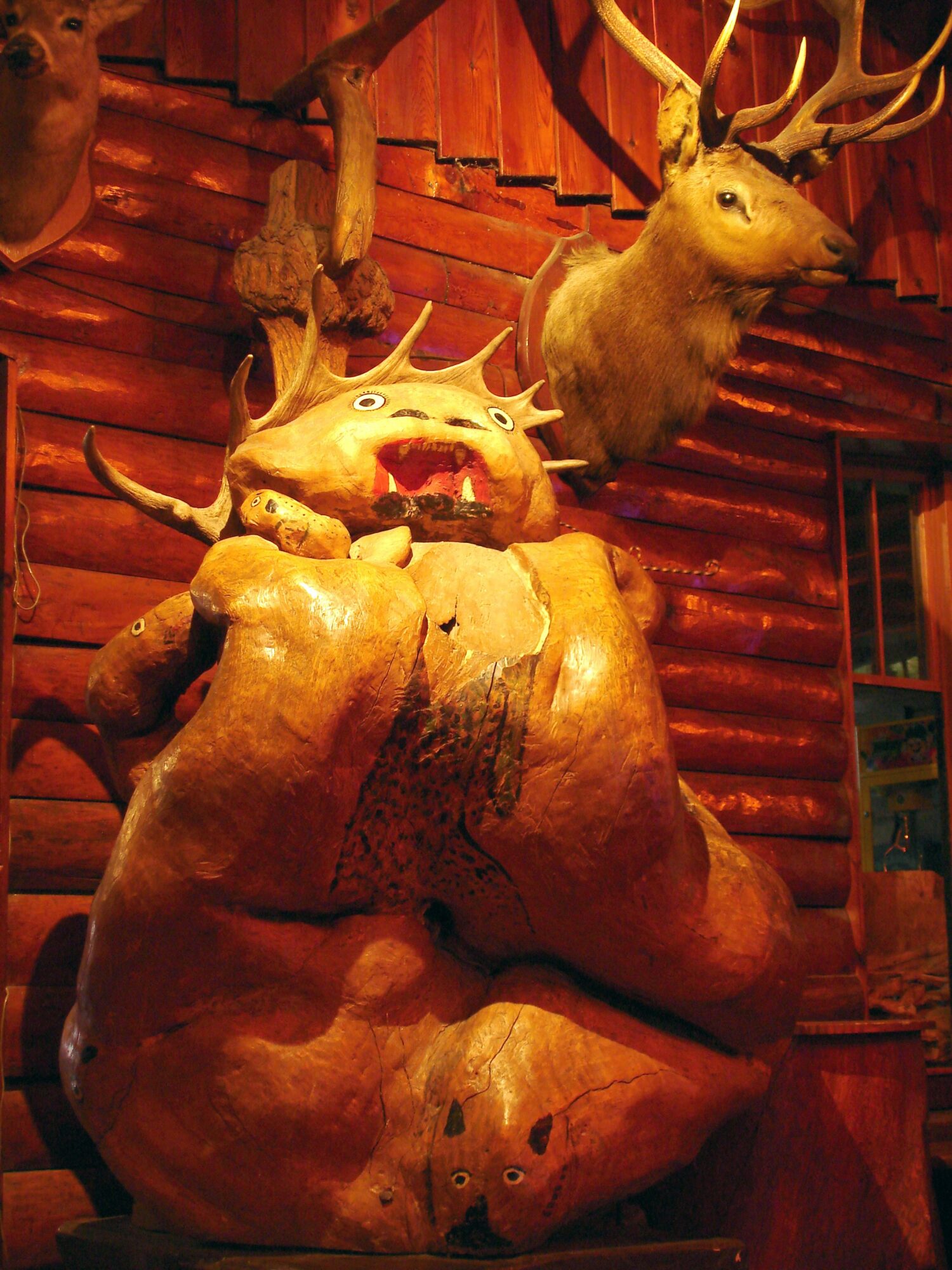 Mounted deer head on wooden wall with a large bear sculpture below, in a rustic setting.