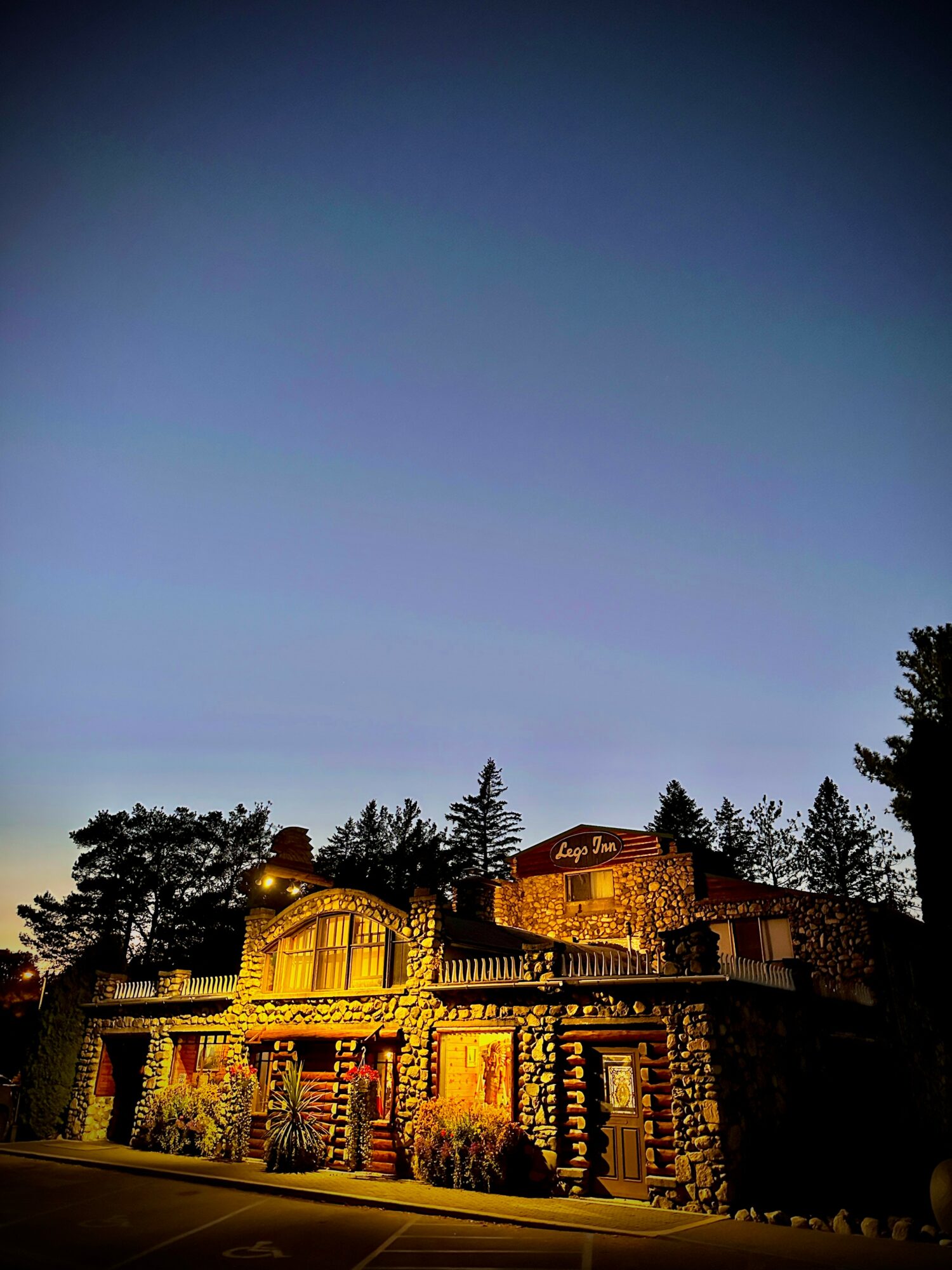 A large house with stone walls and multiple levels, illuminated at night, surrounded by trees under a dark sky.