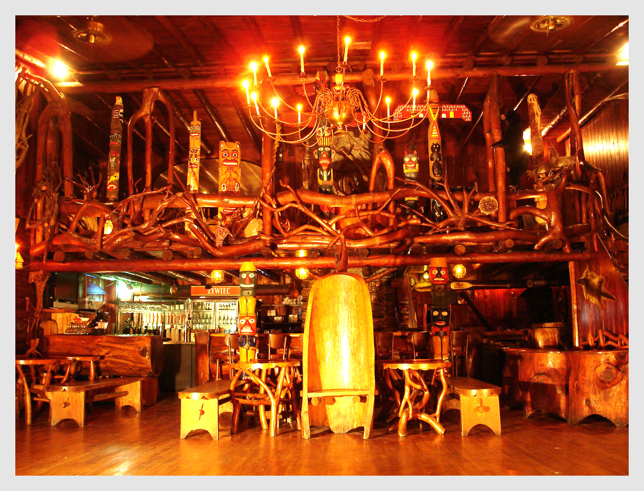 Interior of a bar or restaurant with warm lighting, chandeliers, wooden furniture, and decorative elements, creating a cozy atmosphere.