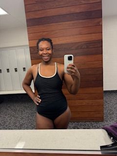 Woman taking a mirror selfie in a room with wooden wall and white door, wearing black athletic wear.