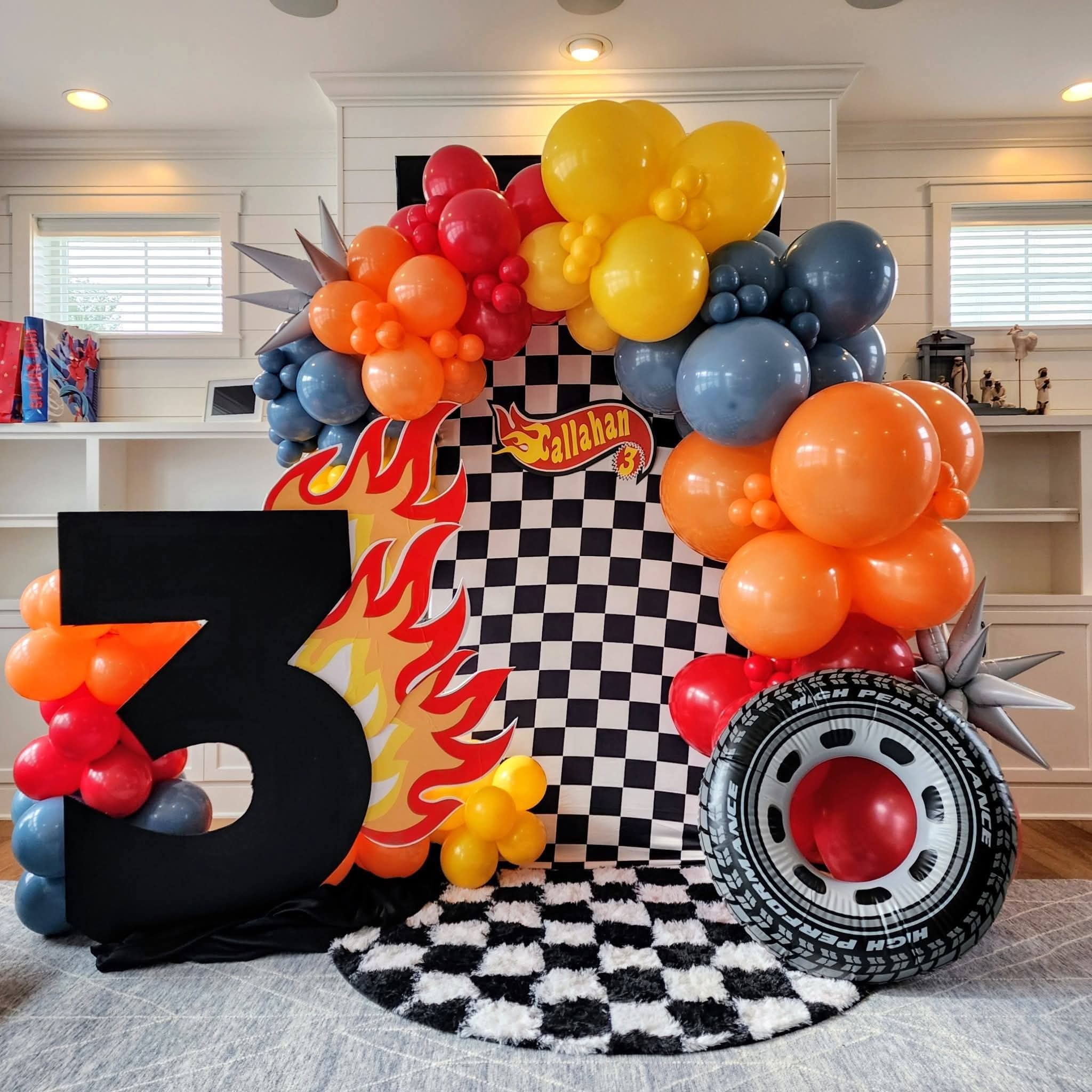 Balloon display with checkered pattern, large number three, and racing-themed decorations in a room.