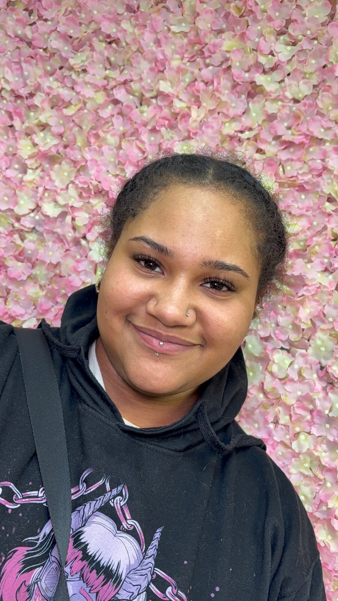 Person smiling in front of a pink and white floral background
