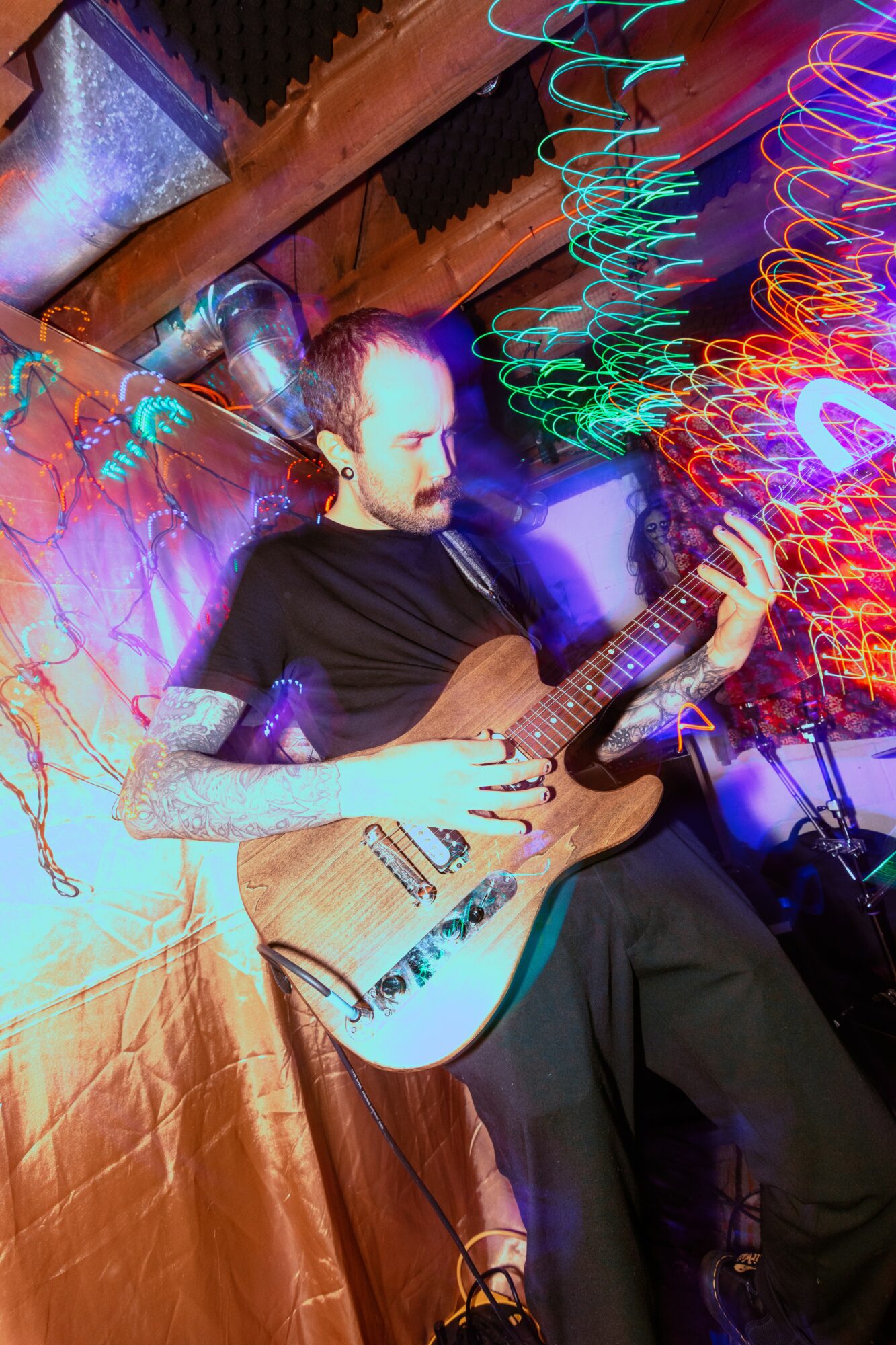 Person playing an acoustic guitar in a colorful, vibrant setting with swirling lights and decorations.