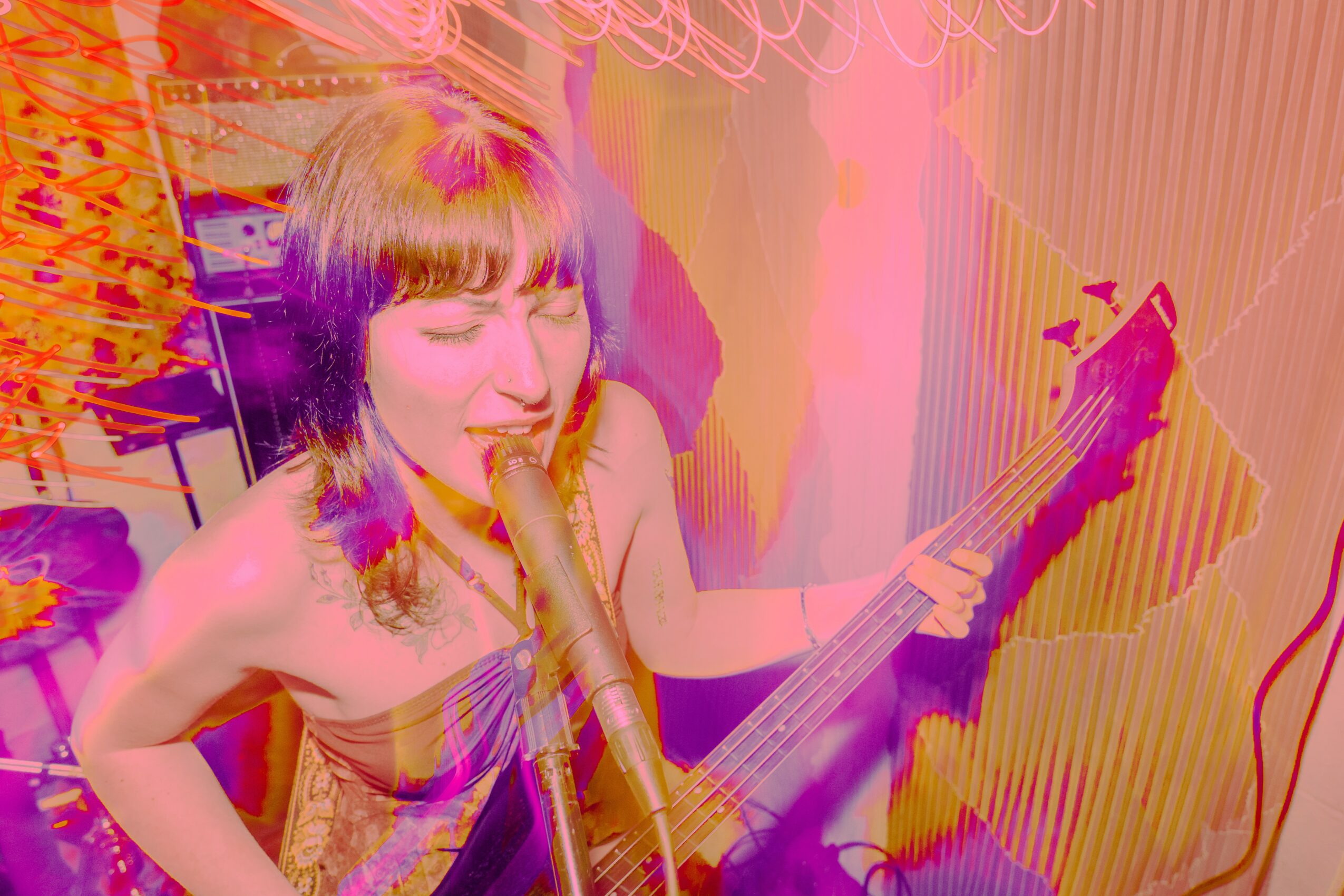 Person with short hair playing guitar and singing into a microphone in a colorful room.