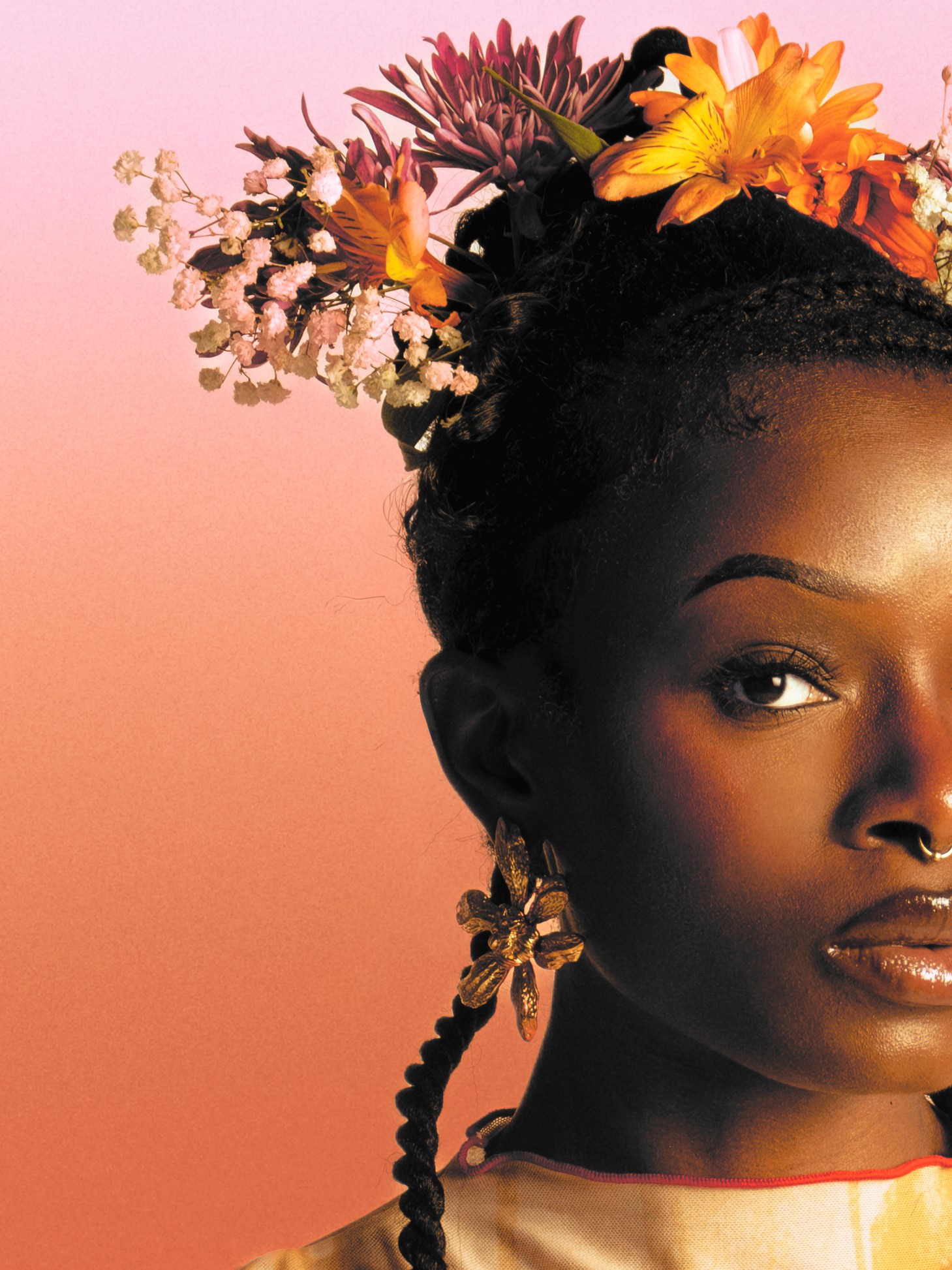Close-up of a woman with floral hair accessories and braided hair, against a pink background.