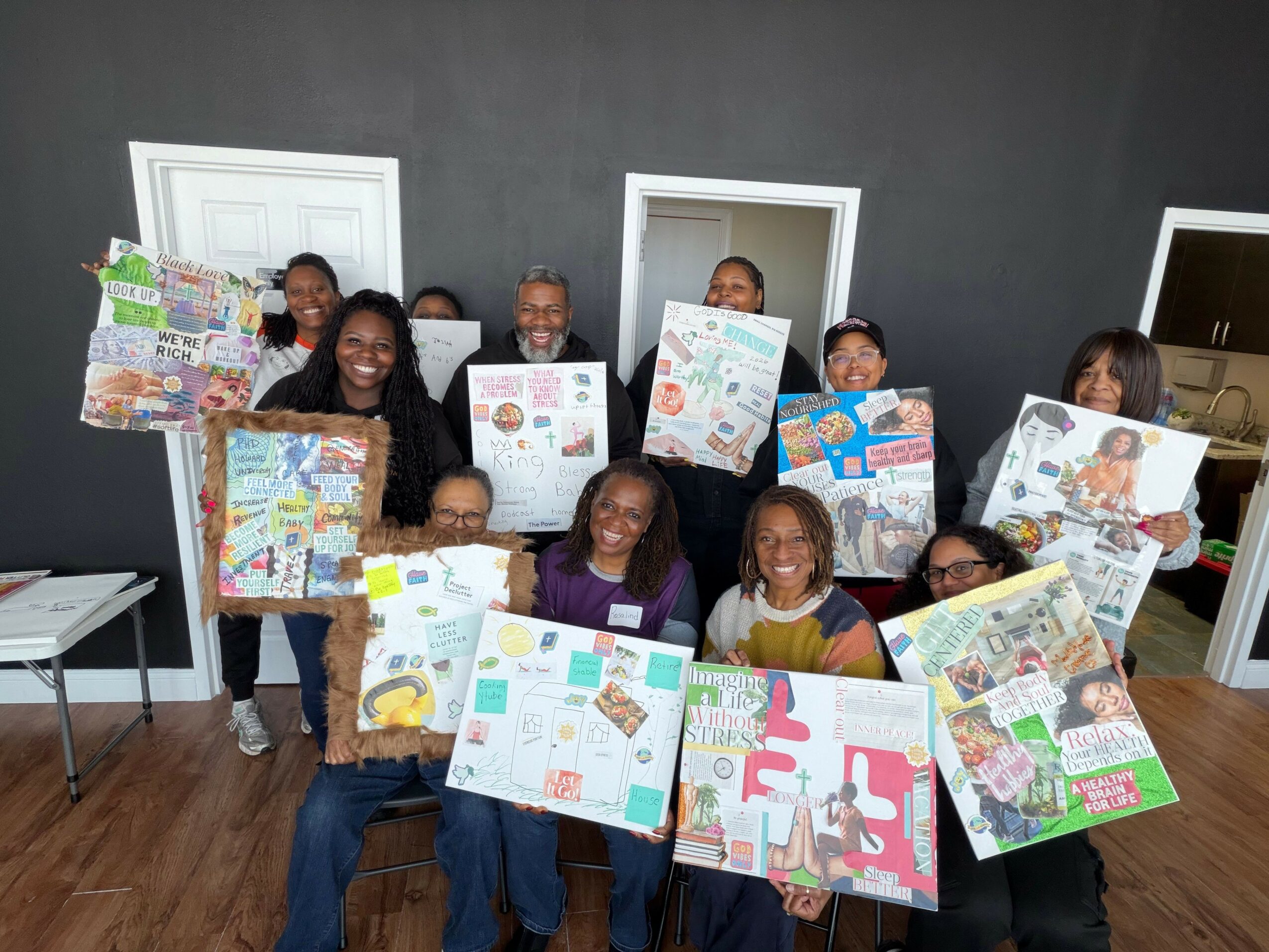 Group of children and adults displaying colorful posters in a room with dark walls and wooden floor.