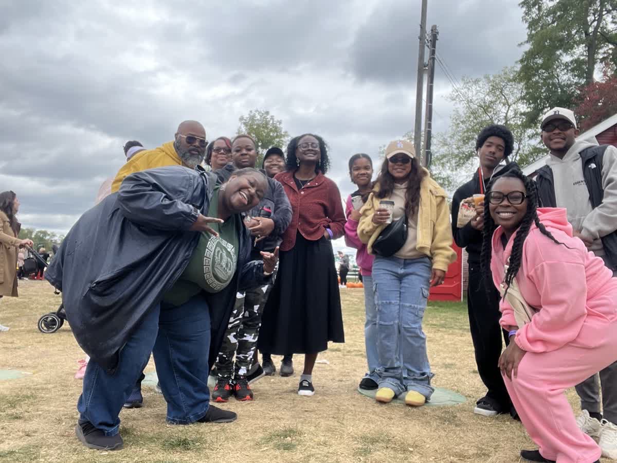 Group of people outdoors on cloudy day, some smiling and posing for photo, with trees and sky in background.