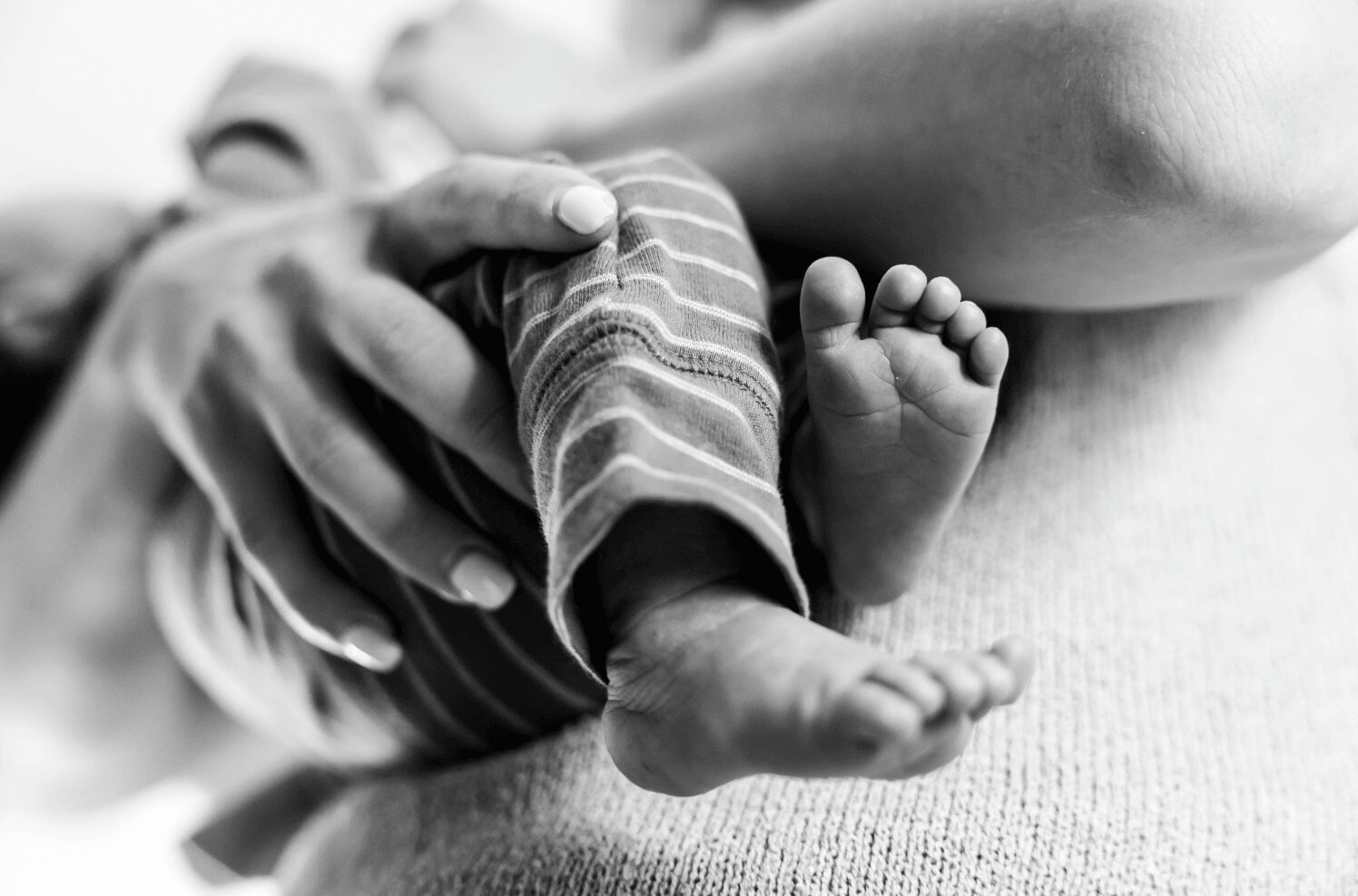 Close-up of an adult holding a newborn baby's foot, with the baby's tiny toes visible, in black and white.