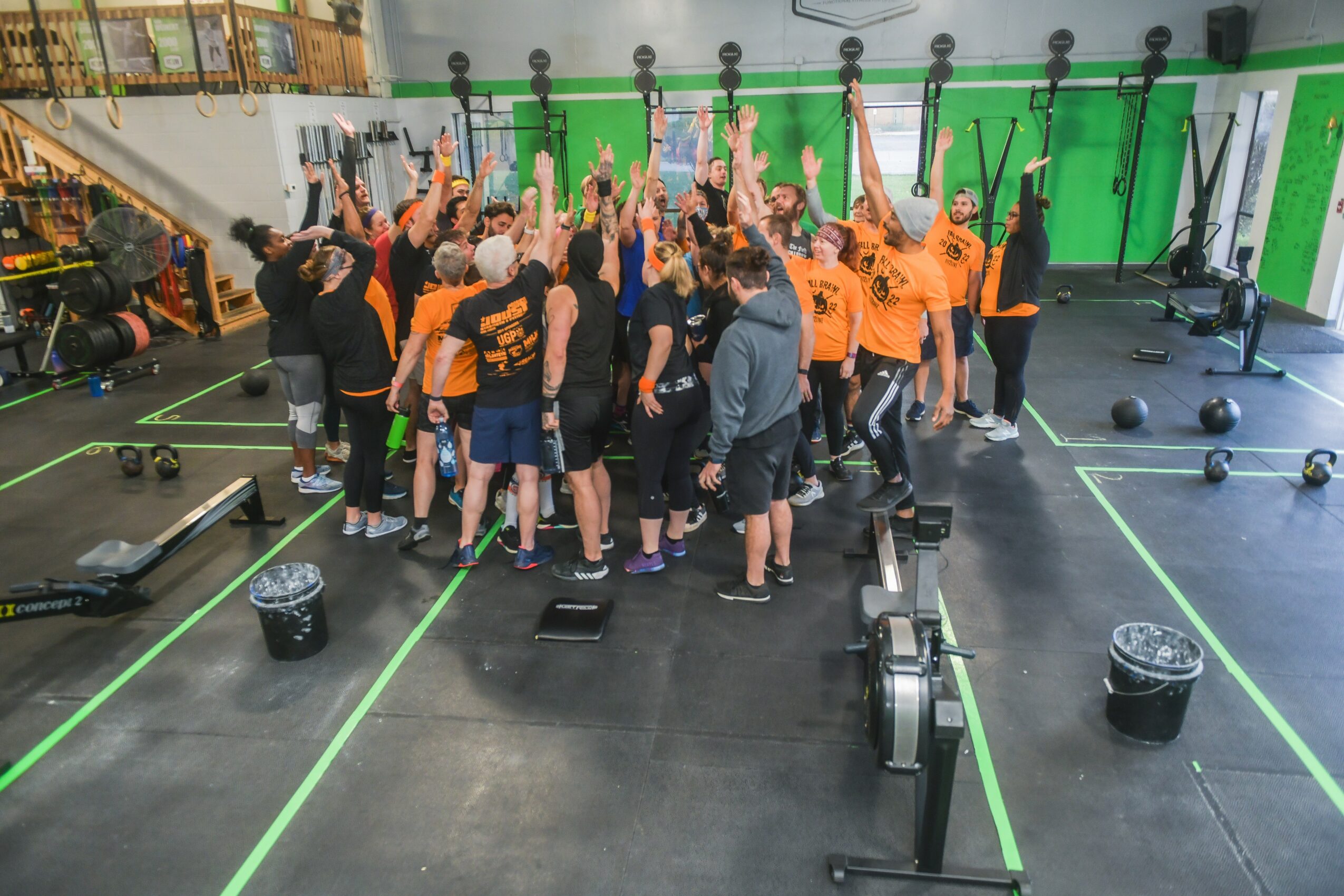 Group of people in a gym raising their hands, surrounded by workout equipment and green walls.