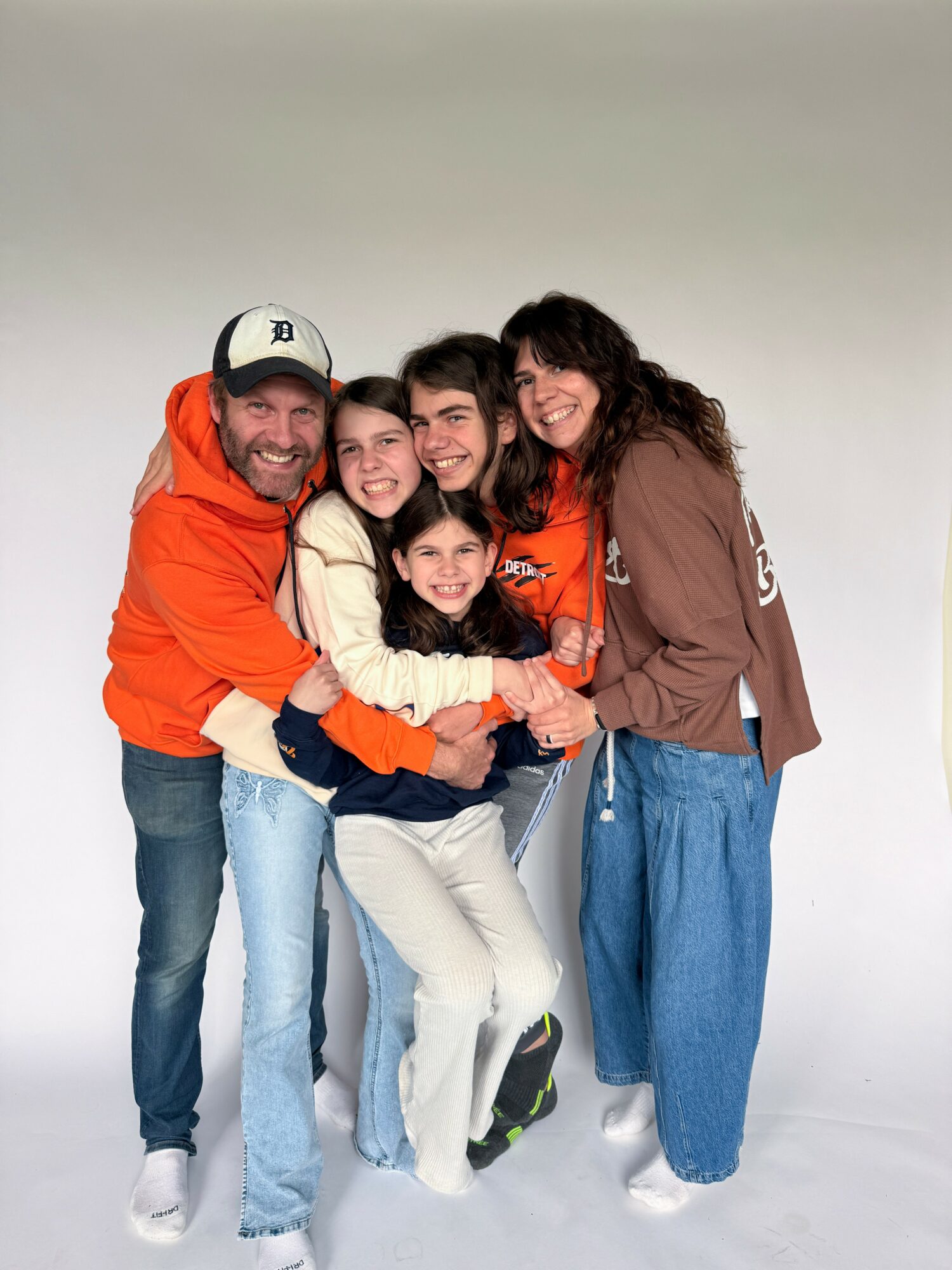 Group of five people smiling and hugging against a plain background.