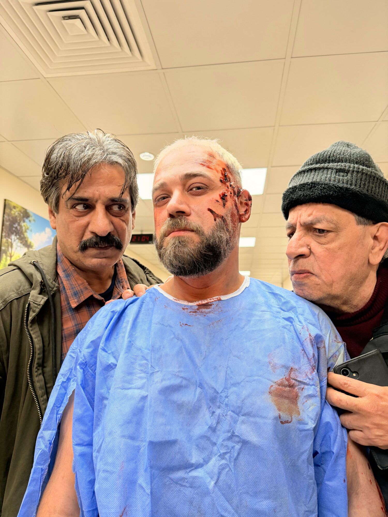 Three men in a room, one in a blue medical gown, two others in casual clothing, all looking at the camera.