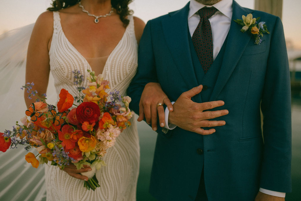 Close-up of a bride and groom, bride holding a colorful bouquet, groom in a teal suit with a boutonniere, wedding attire.