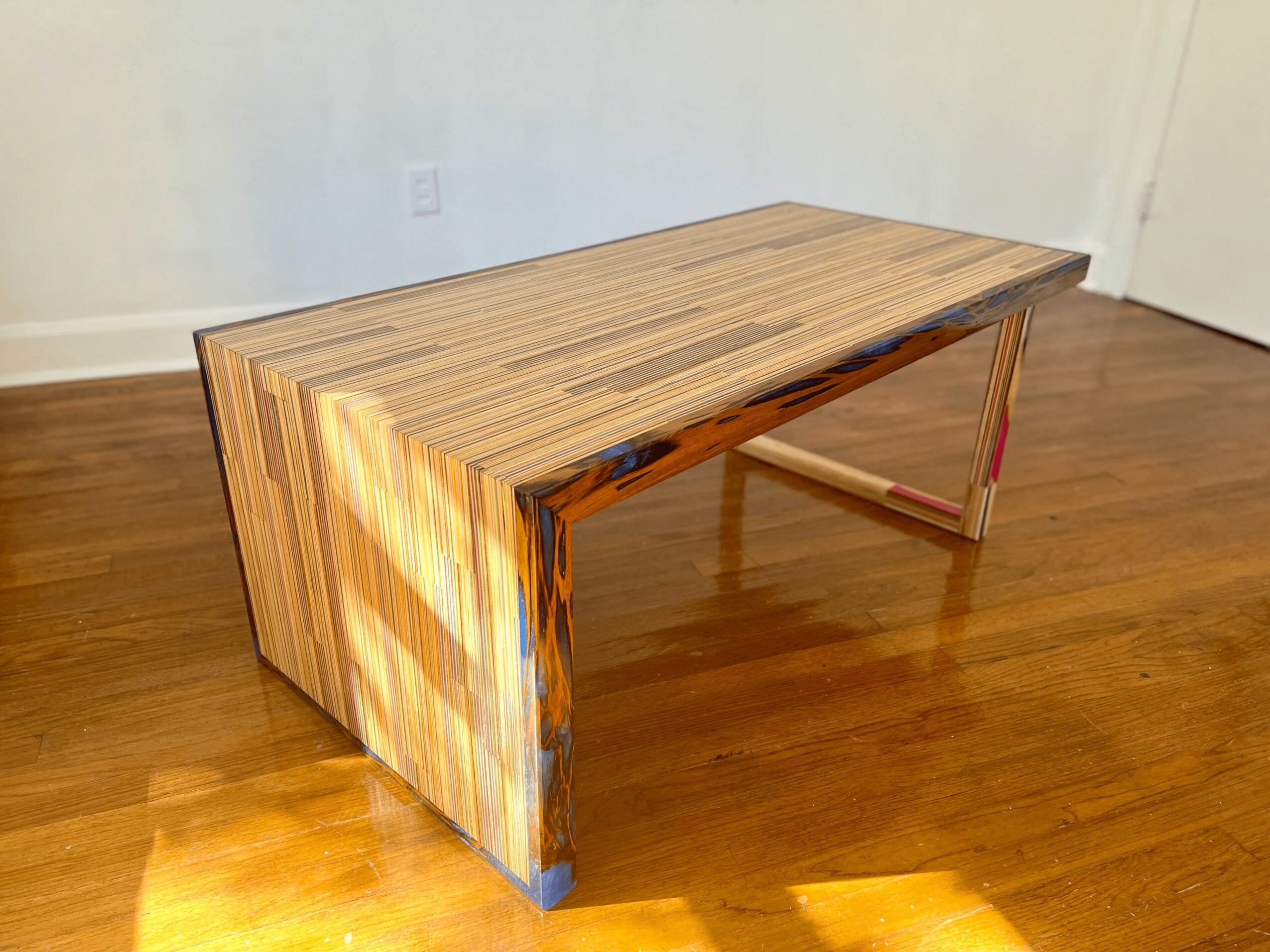 Wooden table with a rectangular top and angled legs on a hardwood floor, against a plain wall.