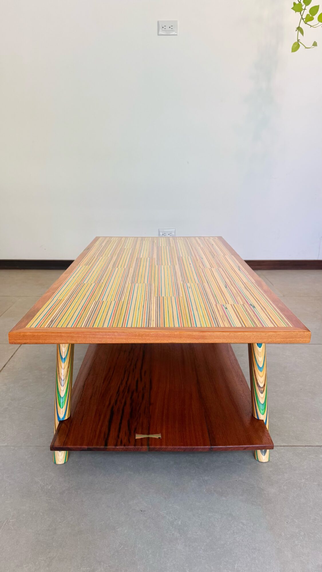 Wooden table with colorful striped top and lower shelf, on a gray floor, against a plain white wall.