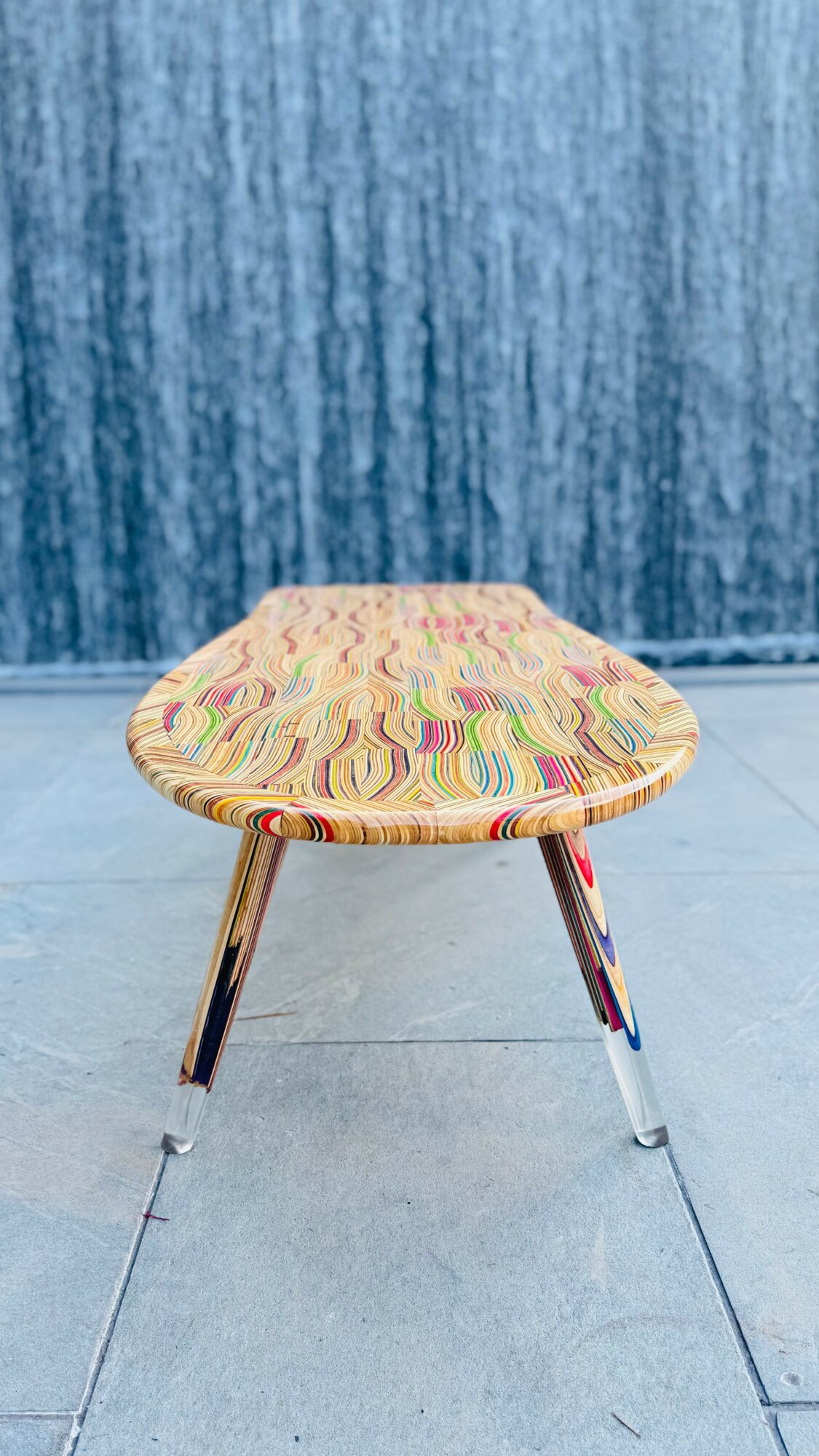 Colorful patterned stool with three metal legs on a tiled floor, blue textured wall in background.