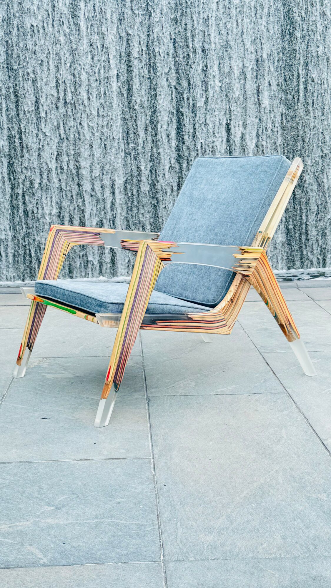 Chair with wooden frame and blue cushions on a tiled floor, against a textured wall background.