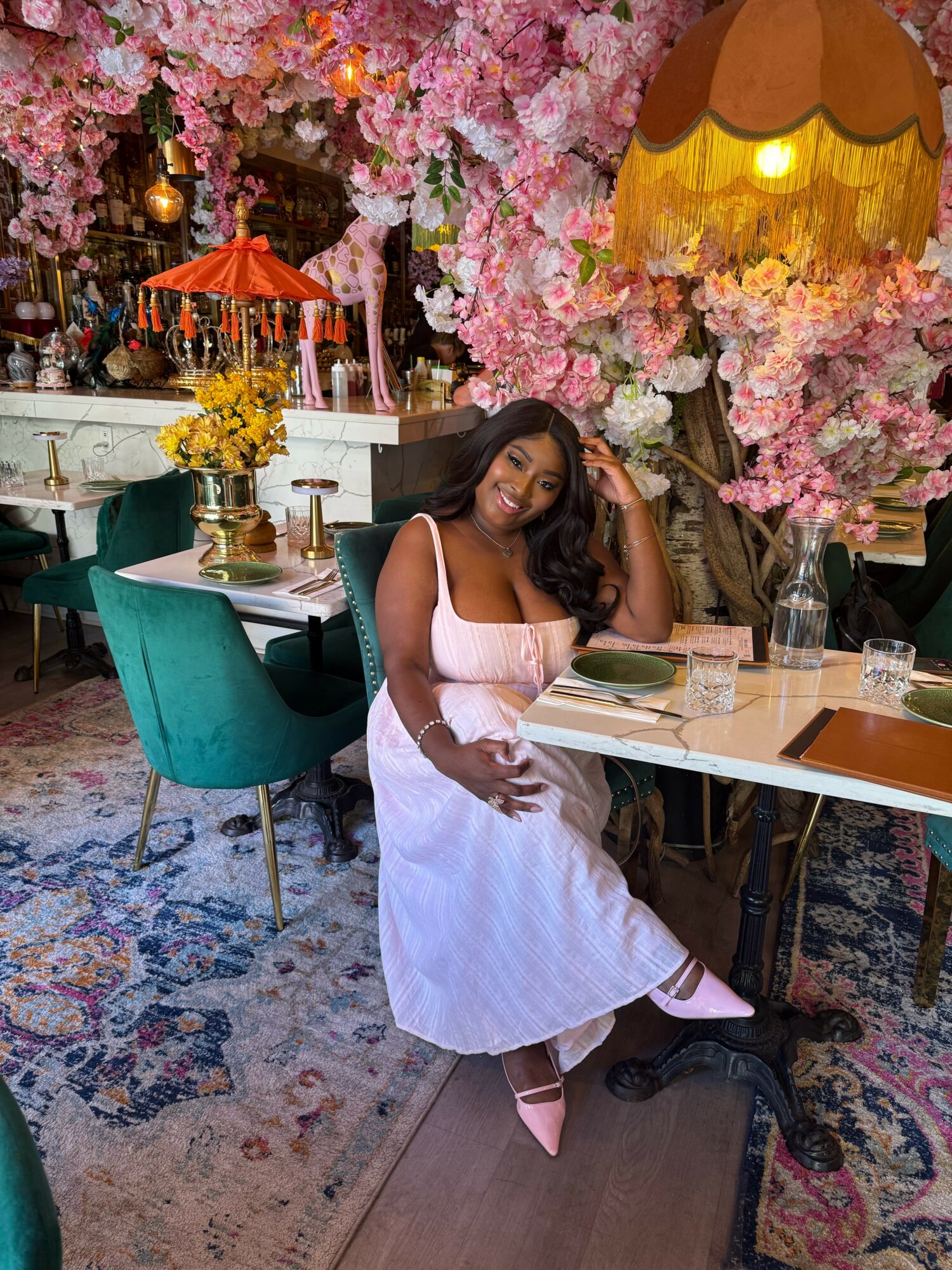 Woman in white dress sitting at a table with pink flowers and decorative umbrellas in background.