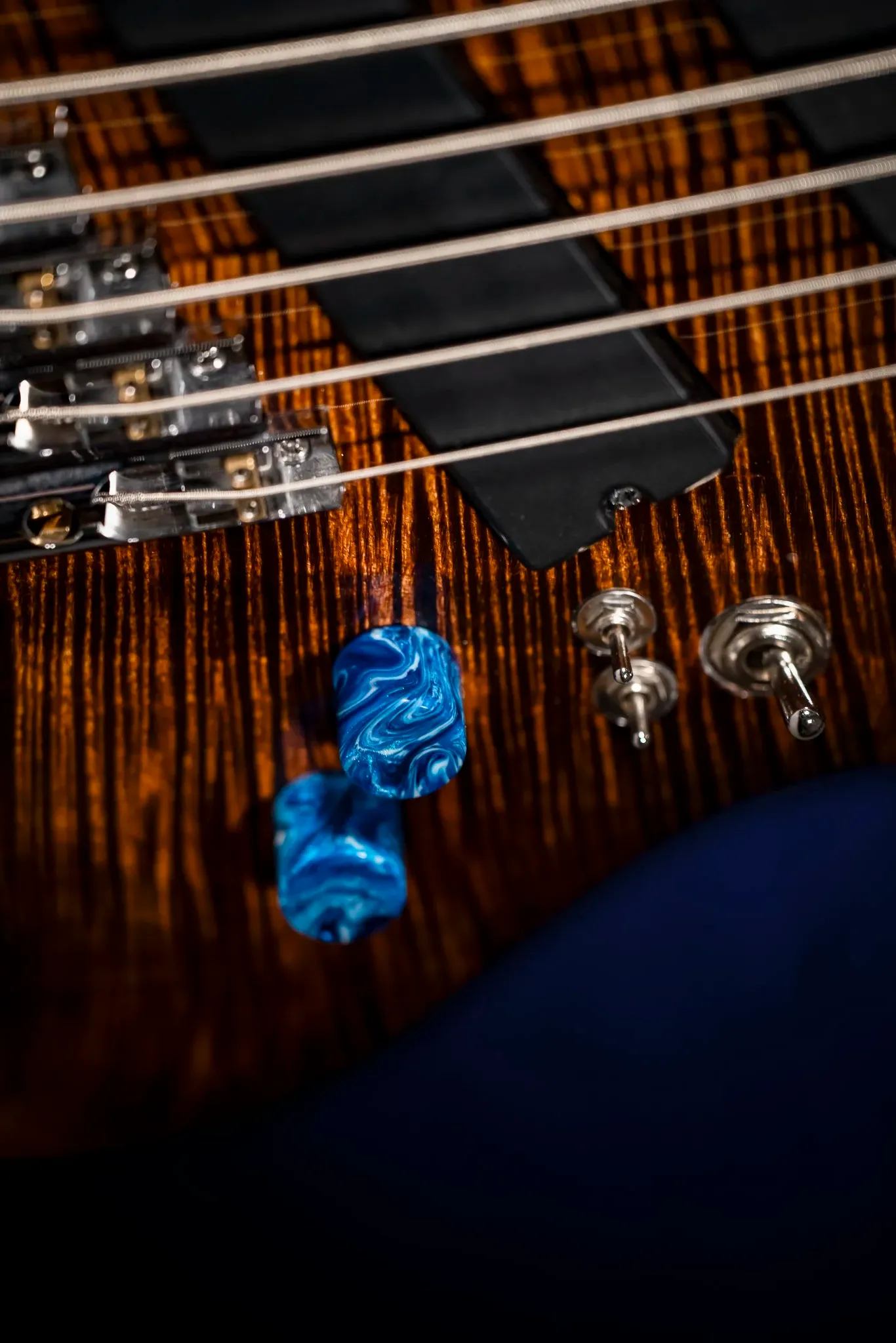Close-up of an electric guitar with a wooden body, strings, and control knobs, with blue guitar picks nearby.