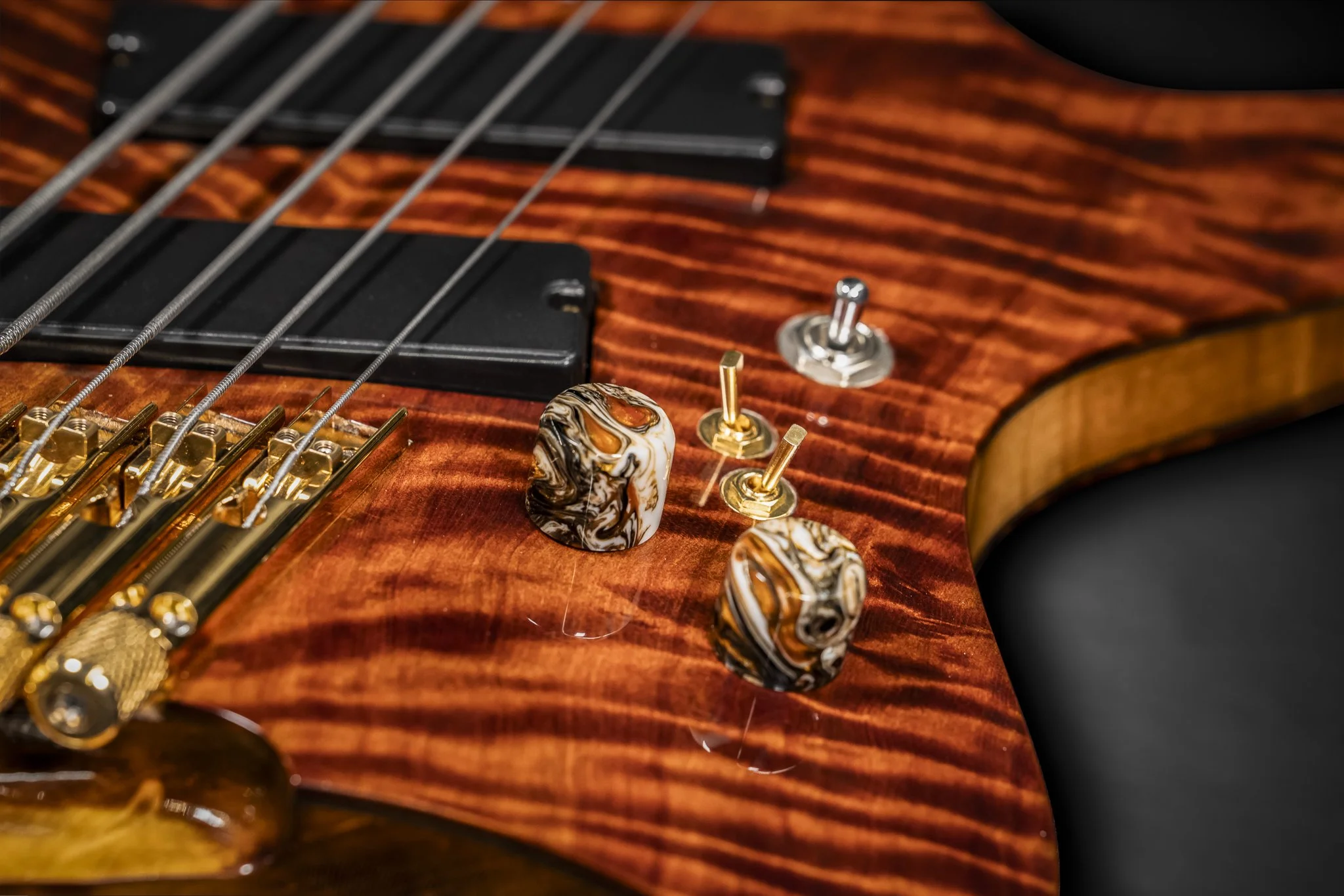 Close-up of a wooden electric bass guitar with tuning pegs and strings, showing detailed wood grain and hardware.