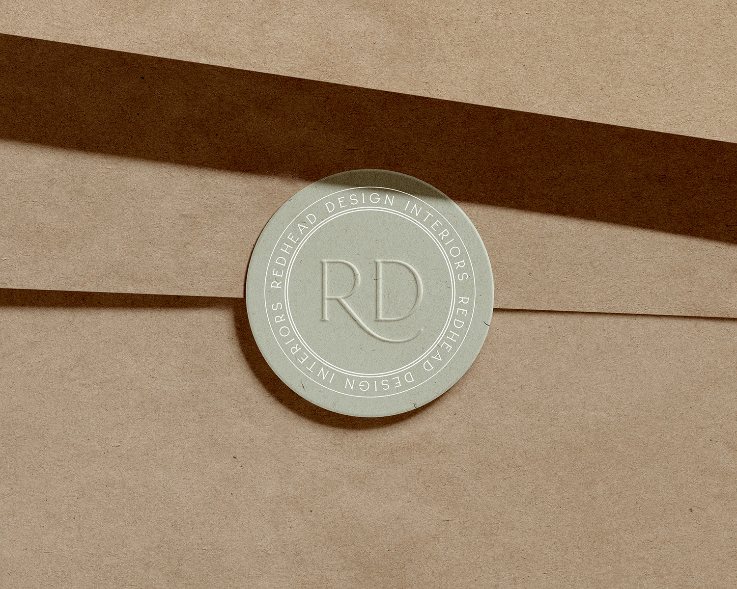 Circular badge with initials 'RD' and text around the edge, placed on layered brown paper surfaces.