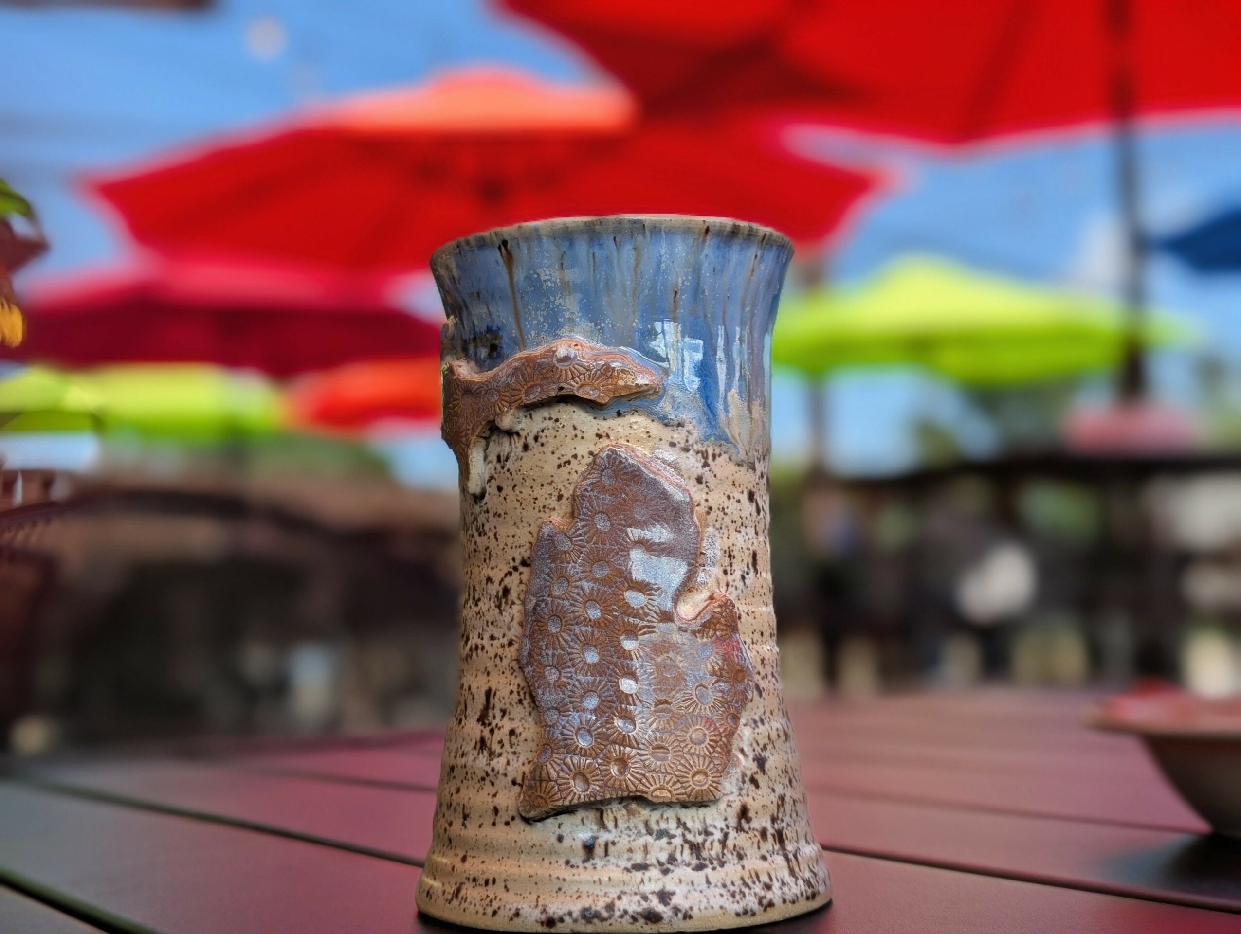 Ceramic cup with a bird design, set on a table with colorful umbrellas in the background.