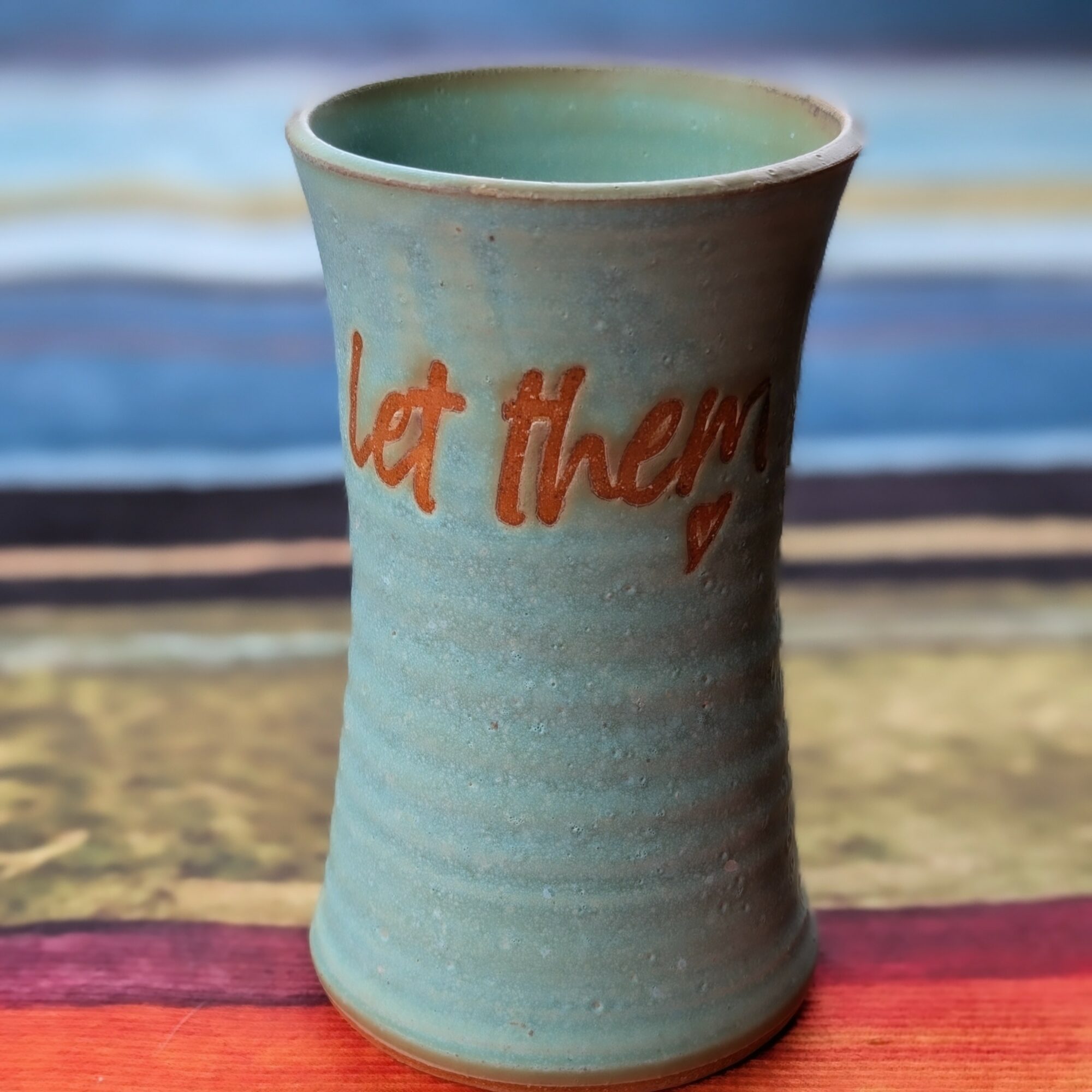 Ceramic cup with orange text, placed on a colorful surface, with a blurred background.