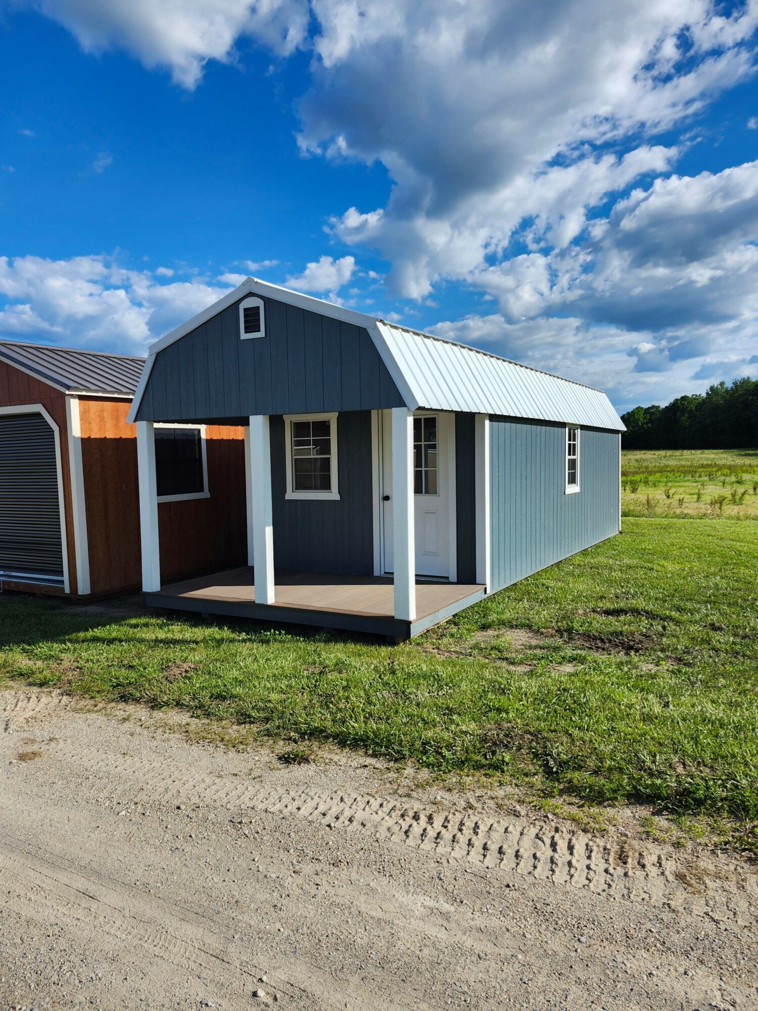 Small modern house with blue and white exterior, surrounded by grass and a dirt path, under a partly cloudy sky.