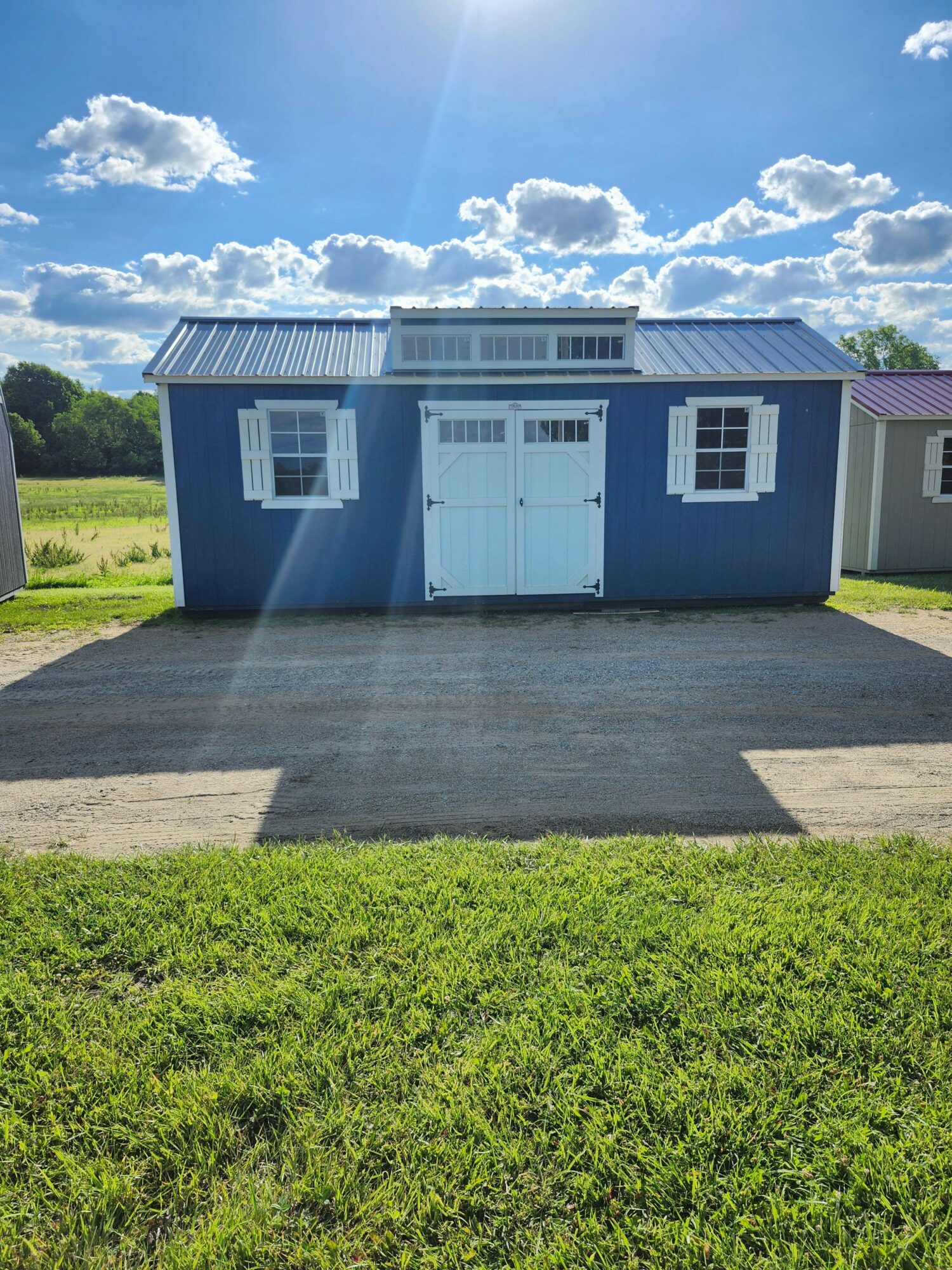Blue house with white garage door, surrounded by green grass and a bright sky with clouds.