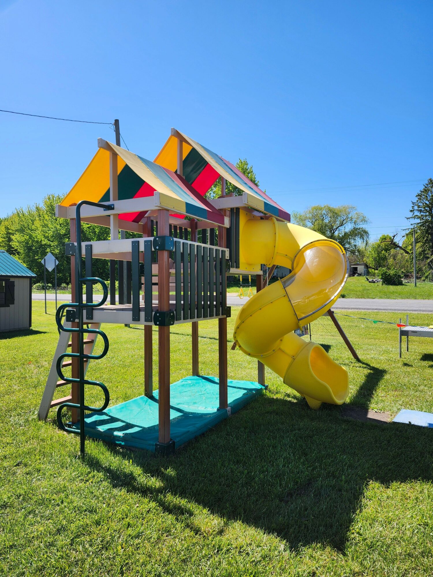 Playground with yellow slide, colorful shade, and green grass under a clear blue sky.