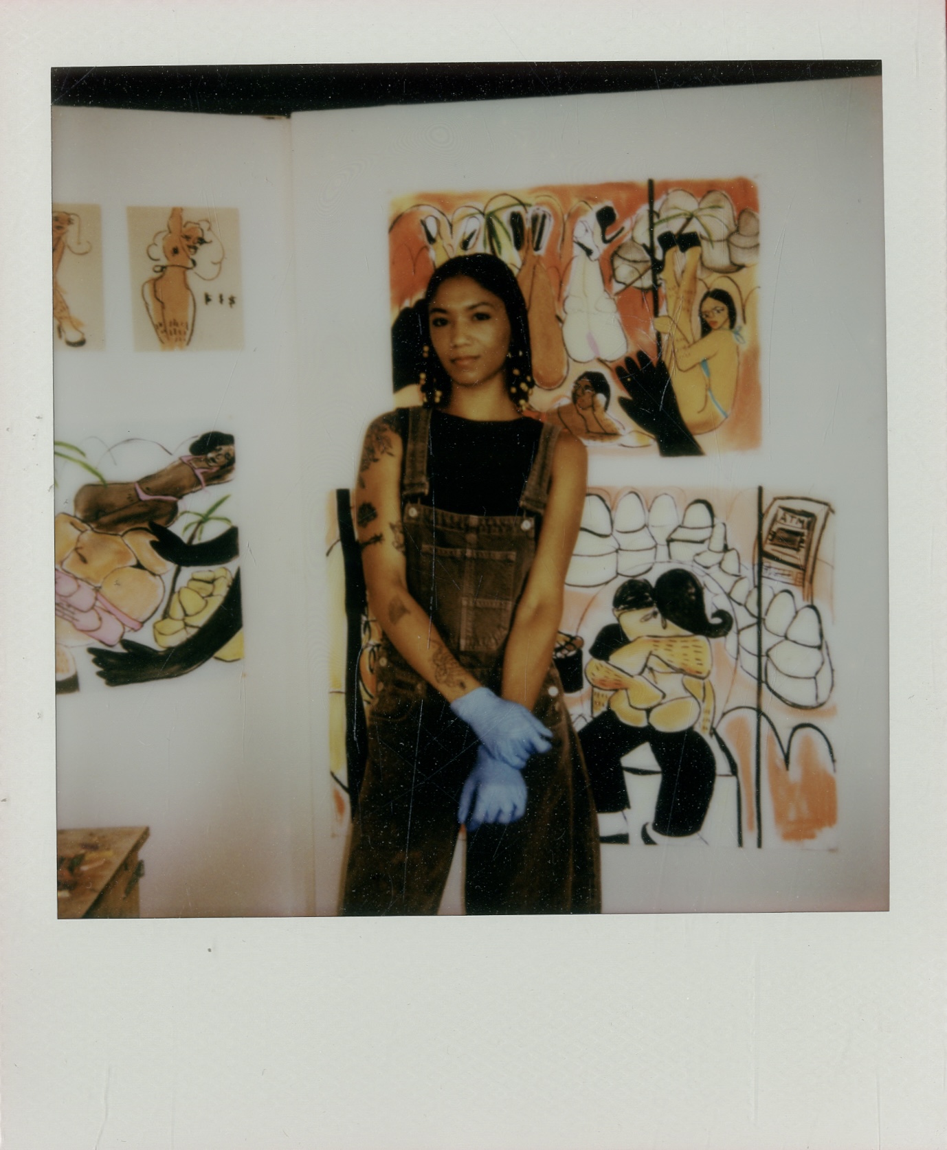 Young woman standing in front of colorful abstract paintings, holding a blue object, in an art gallery or studio setting.
